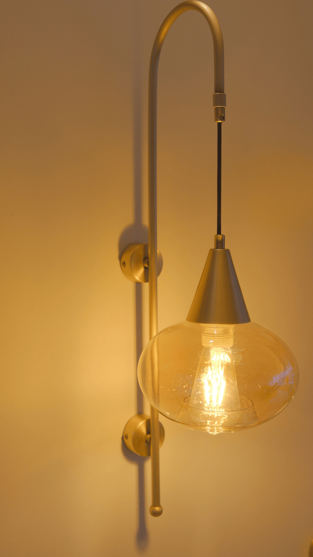 Minimalist brass wall sconce with slender frame and exposed bulb under clear glass shade