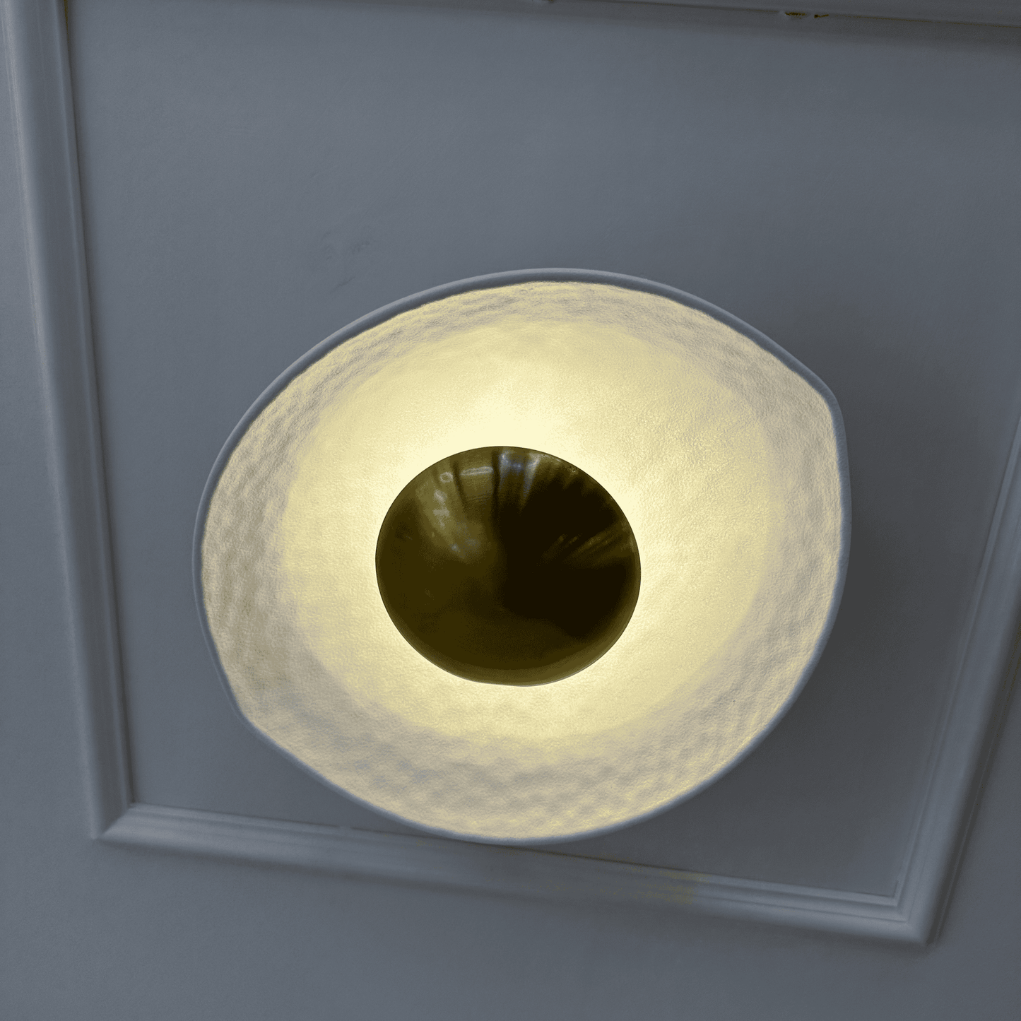 Close-up of a white and gold deco wall sconce with a round hammered finish and central golden dome.