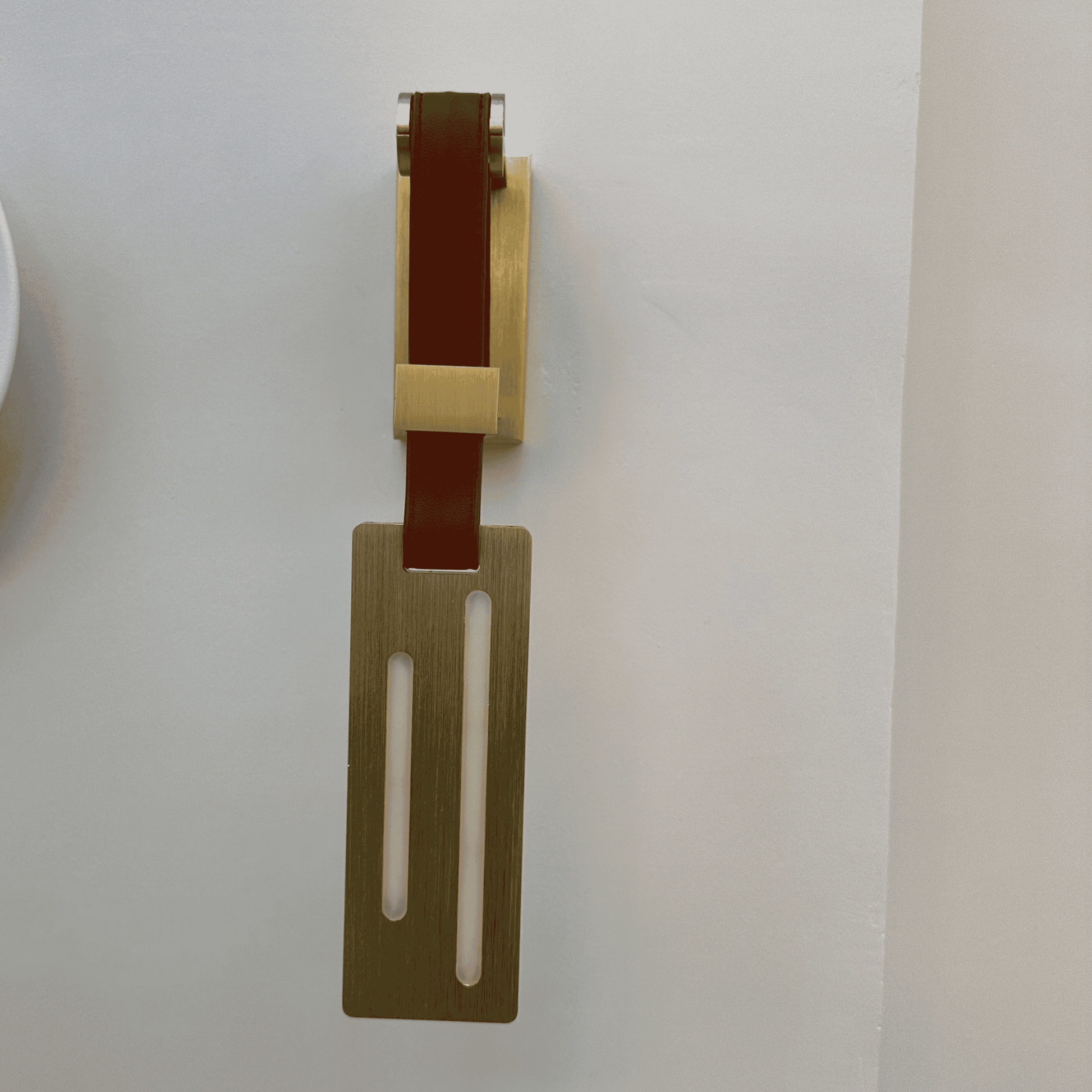 Minimalist leather wall sconce in brushed brass with dual vertical light diffusers.