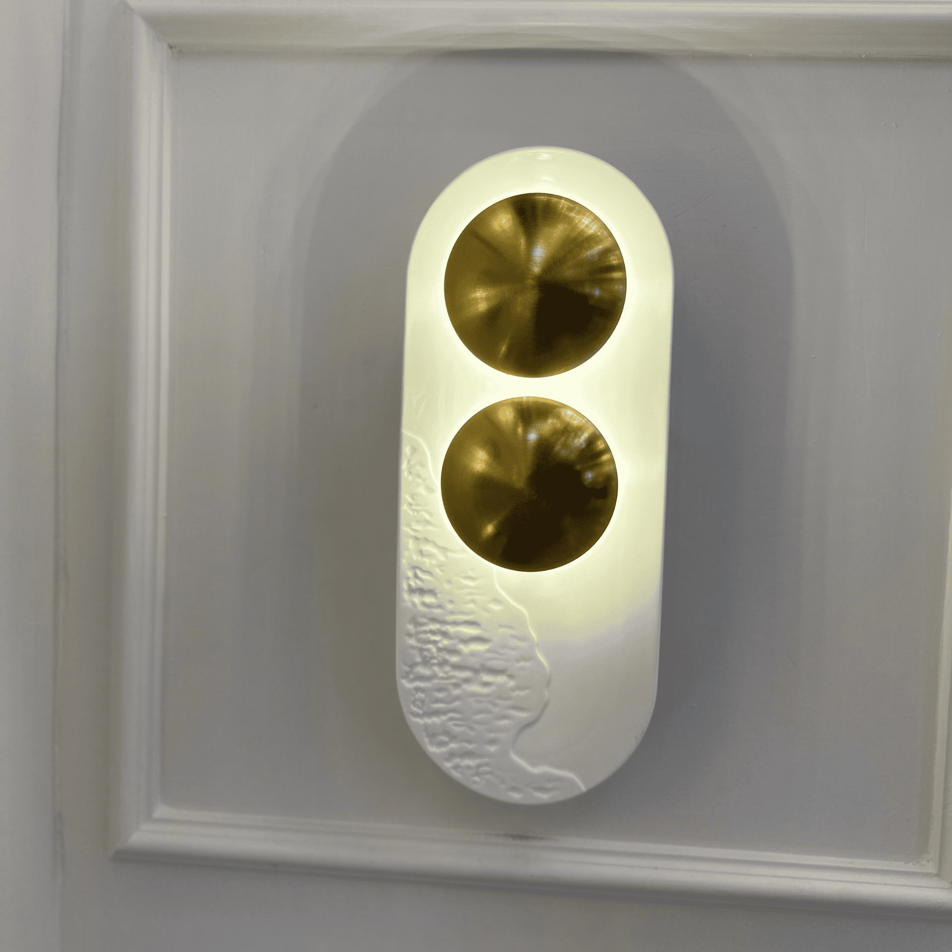 Vertical minimalist LED wall sconce with two brass accents and white resin for modern interiors.