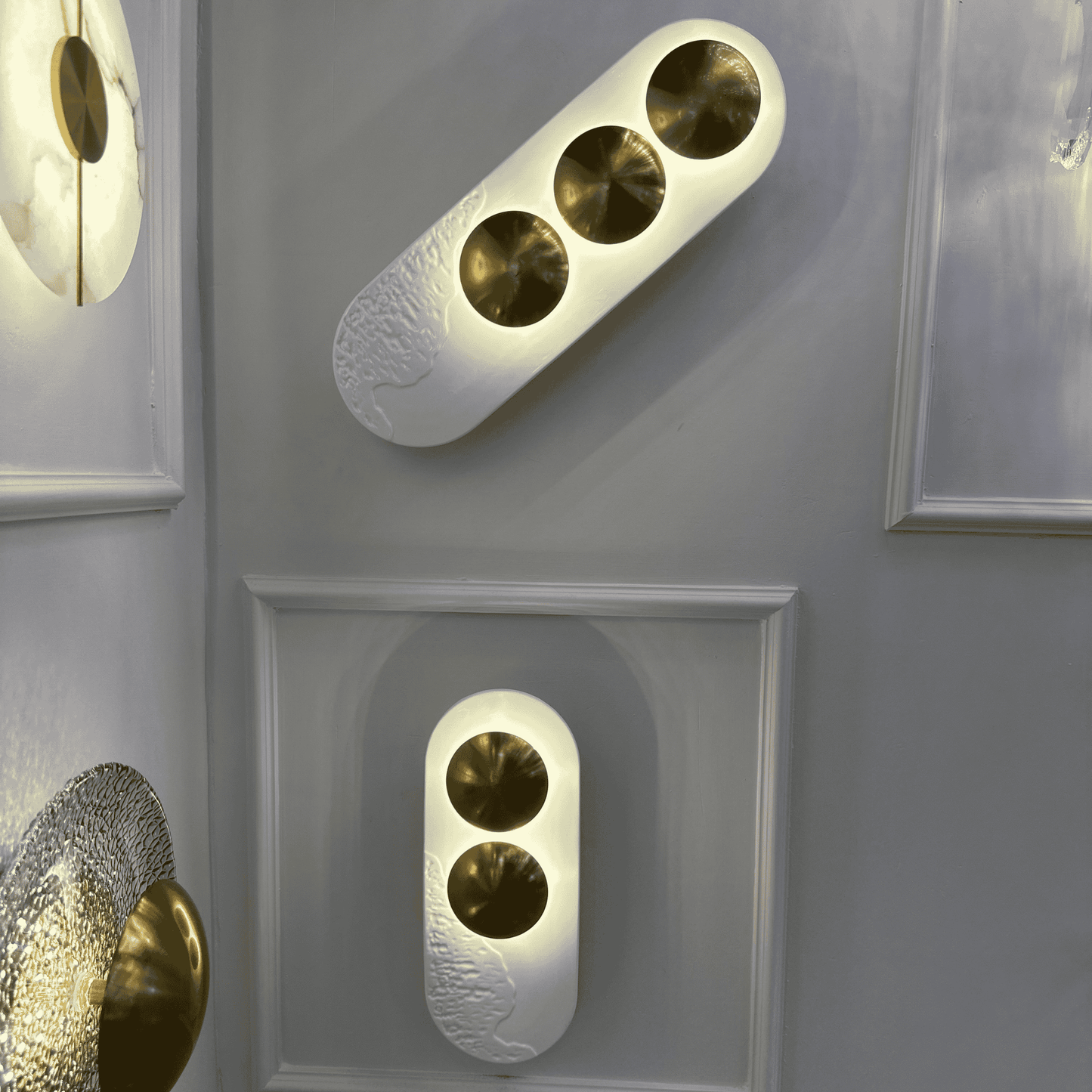 Pair of minimalist LED wall sconces with white resin and brass accents, designed for modern interiors.