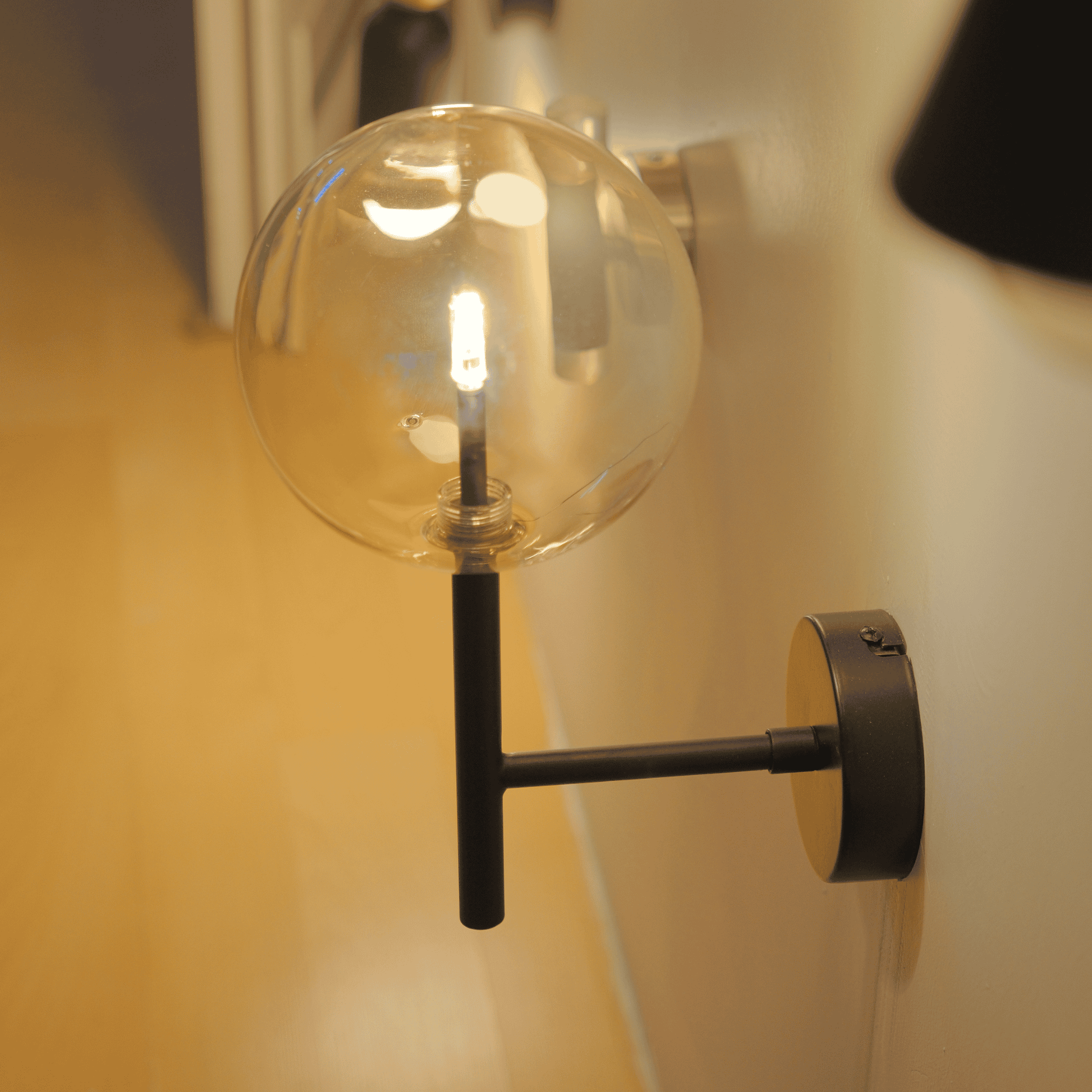 Minimalist black wall sconce with clear globe shade for ambient light.