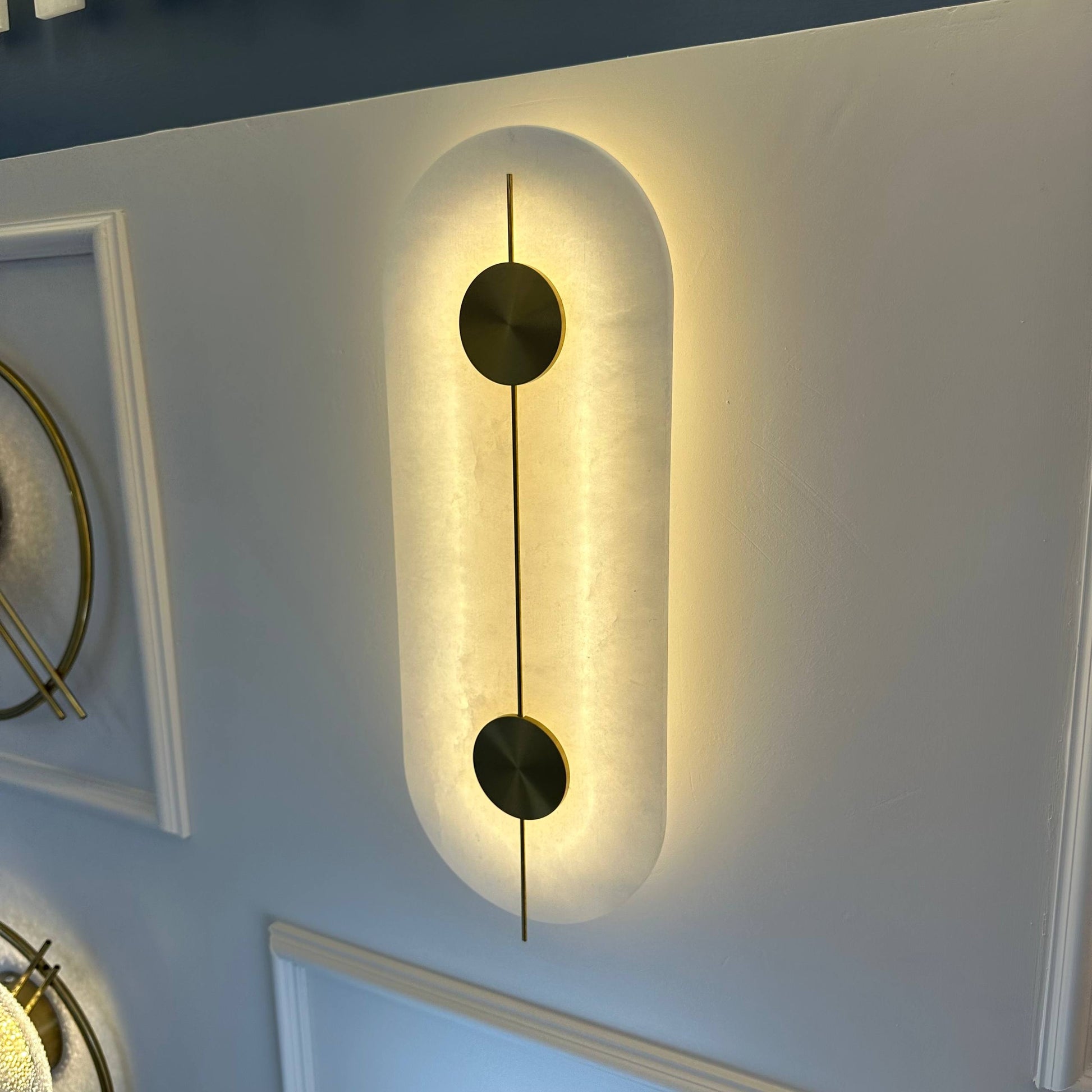 Wall-mounted alabaster sconce with glowing backlight and brass circular accents for contemporary lighting.