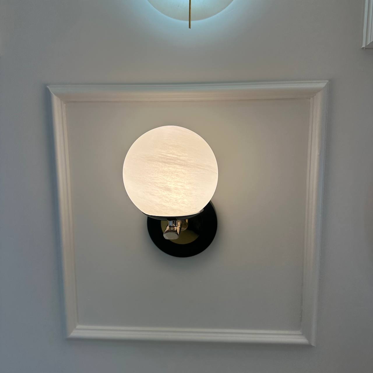Centered alabaster globe wall sconce with black and brass mount on a decorative wall panel.