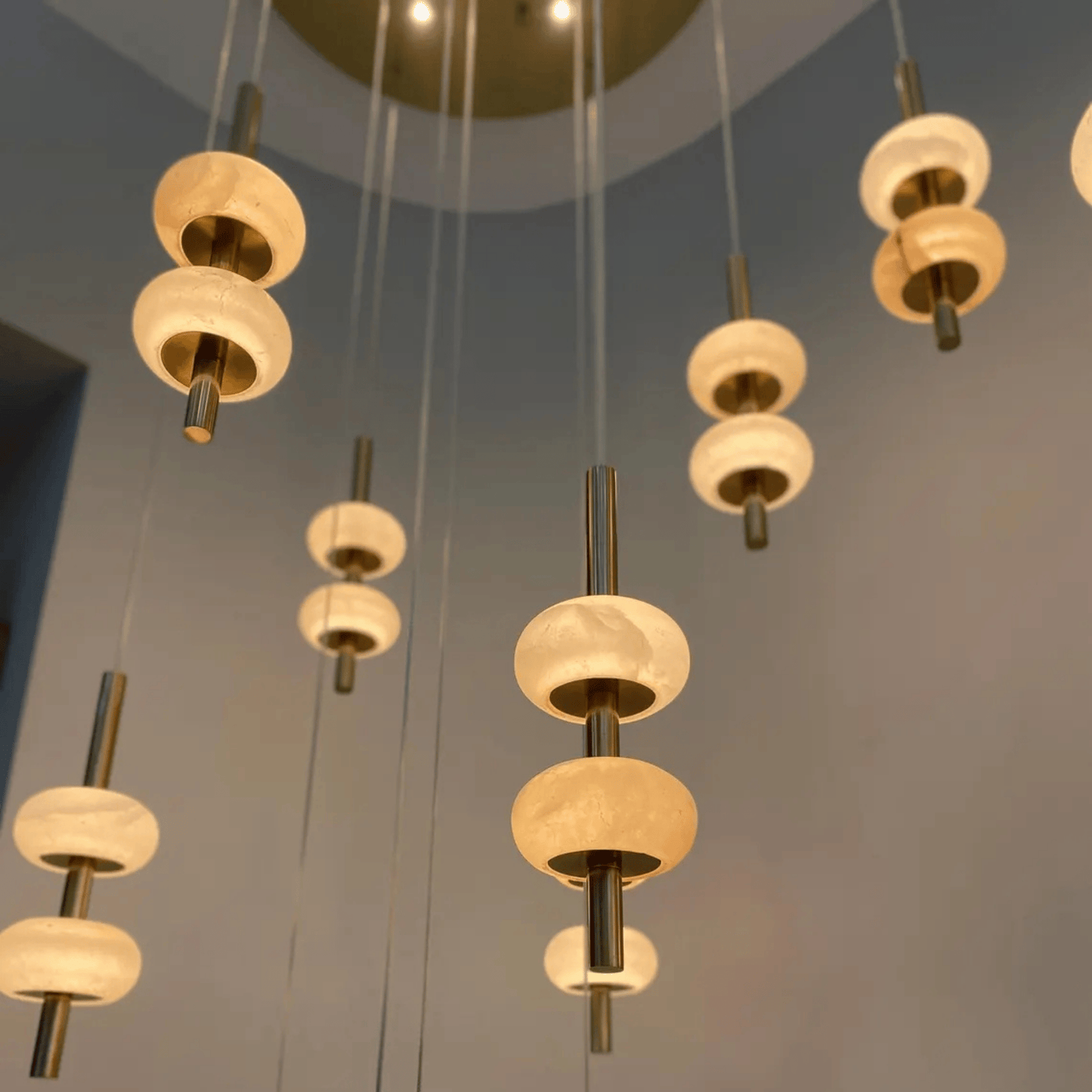 Cluster of alabaster pendant lights with warm glow and brushed brass rods suspended from the ceiling in a modern interior.