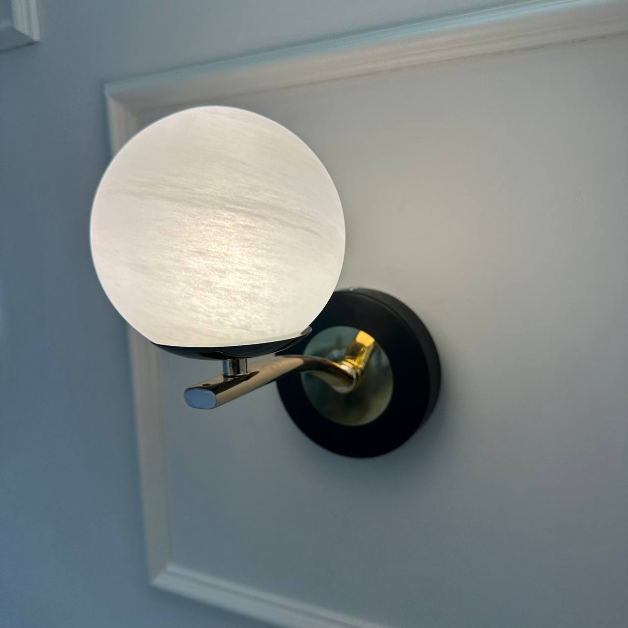 A spherical alabaster wall sconce with black and brass accents emits soft, warm light in a modern interior.