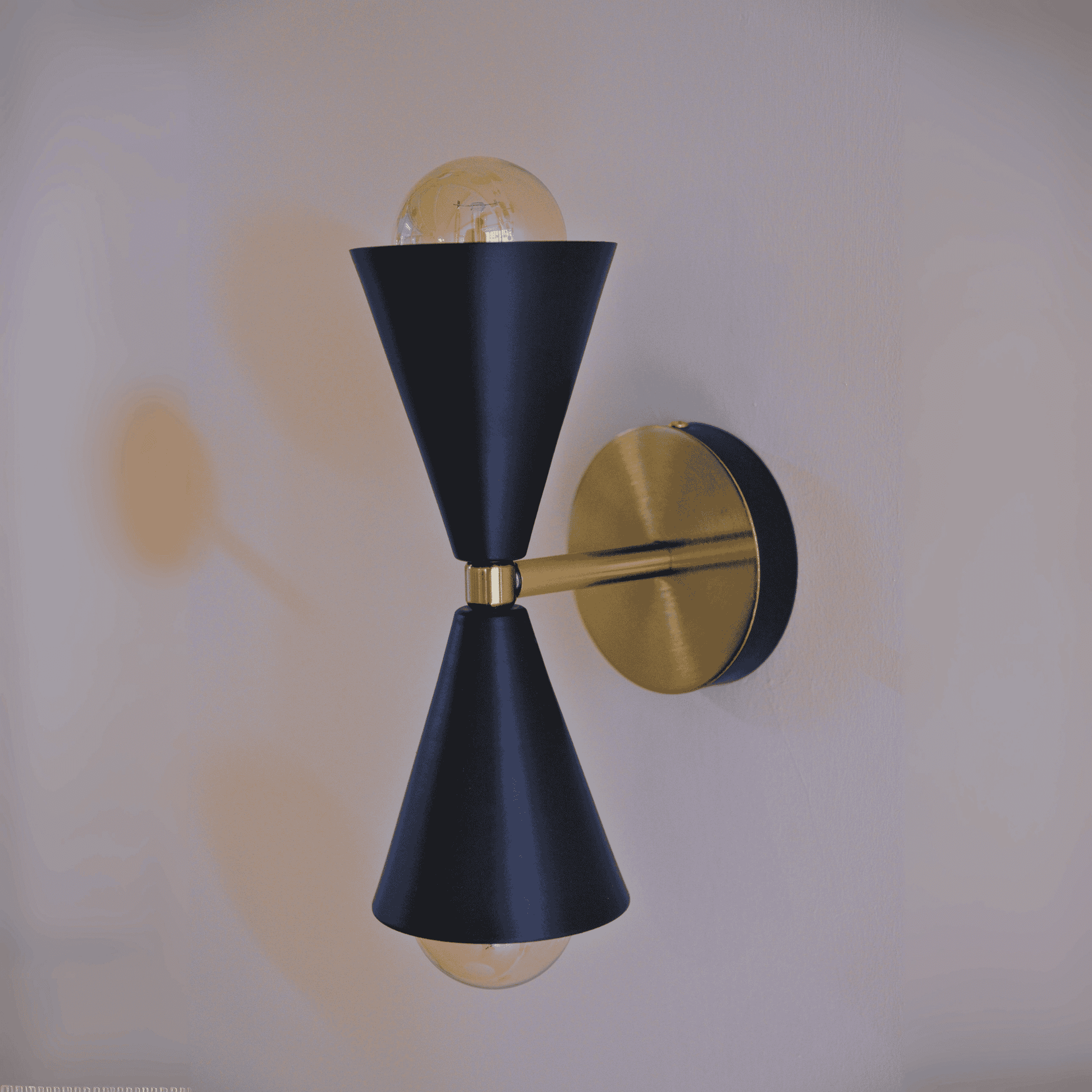 Black and brass double cone wall sconce with exposed bulbs mounted on a white wall for modern interior lighting.
