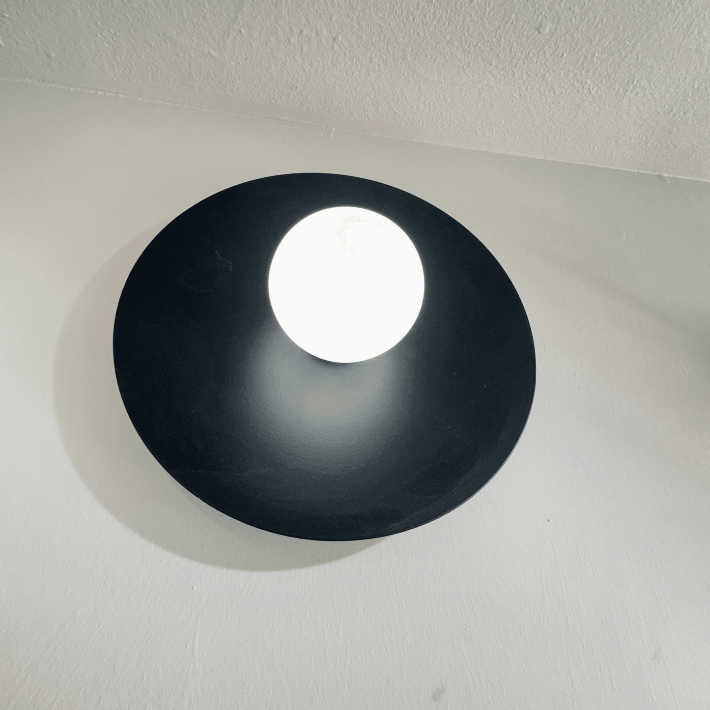 Angular view of modern black disc wall light mounted on a white wall for ambient interior lighting.