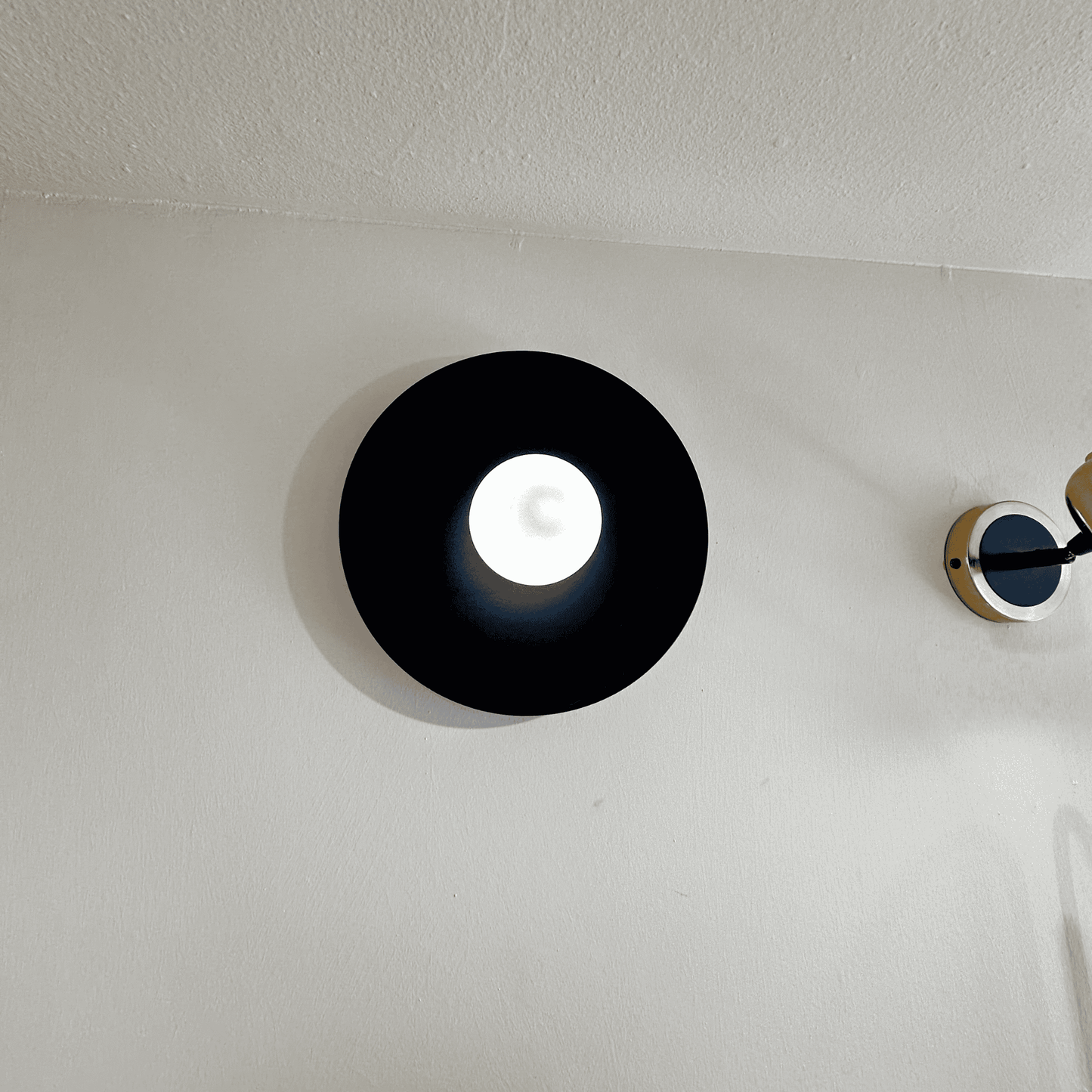 Modern black disc wall sconce with soft central glow mounted on a neutral interior wall.