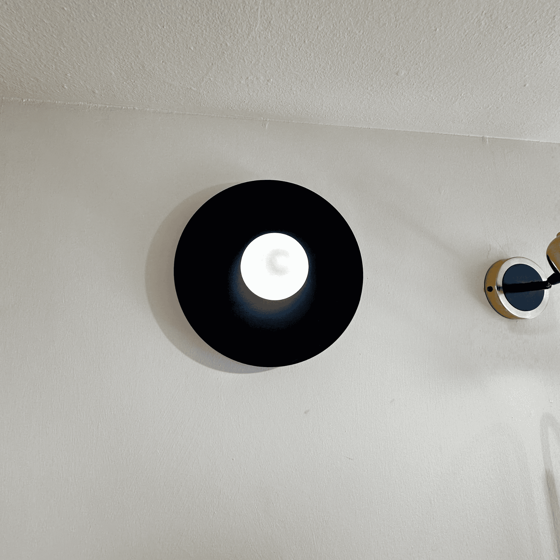 Modern black disc wall sconce with soft central glow mounted on a neutral interior wall.