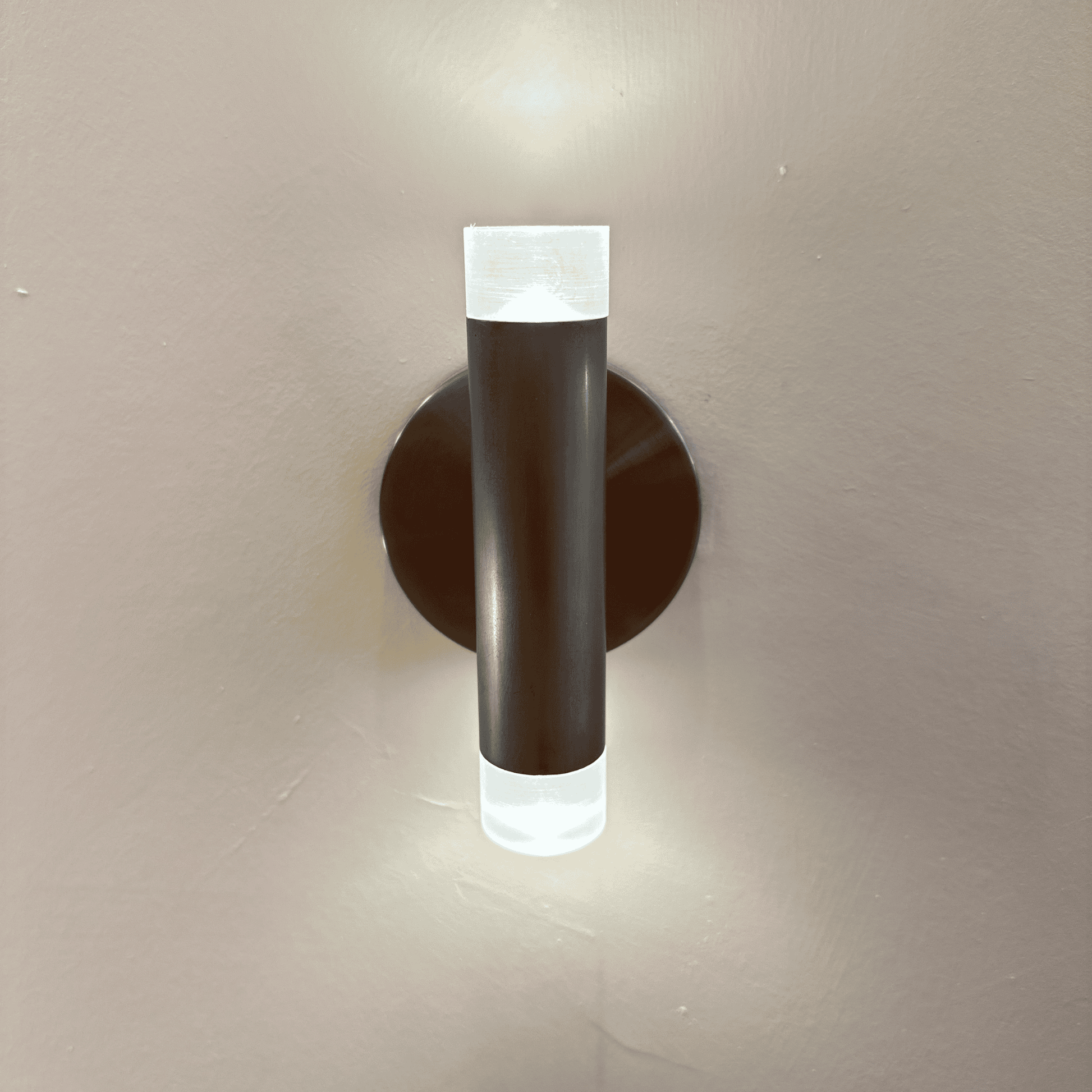Modern black LED wall sconce with cylindrical design emitting light from both ends, mounted on a neutral wall.