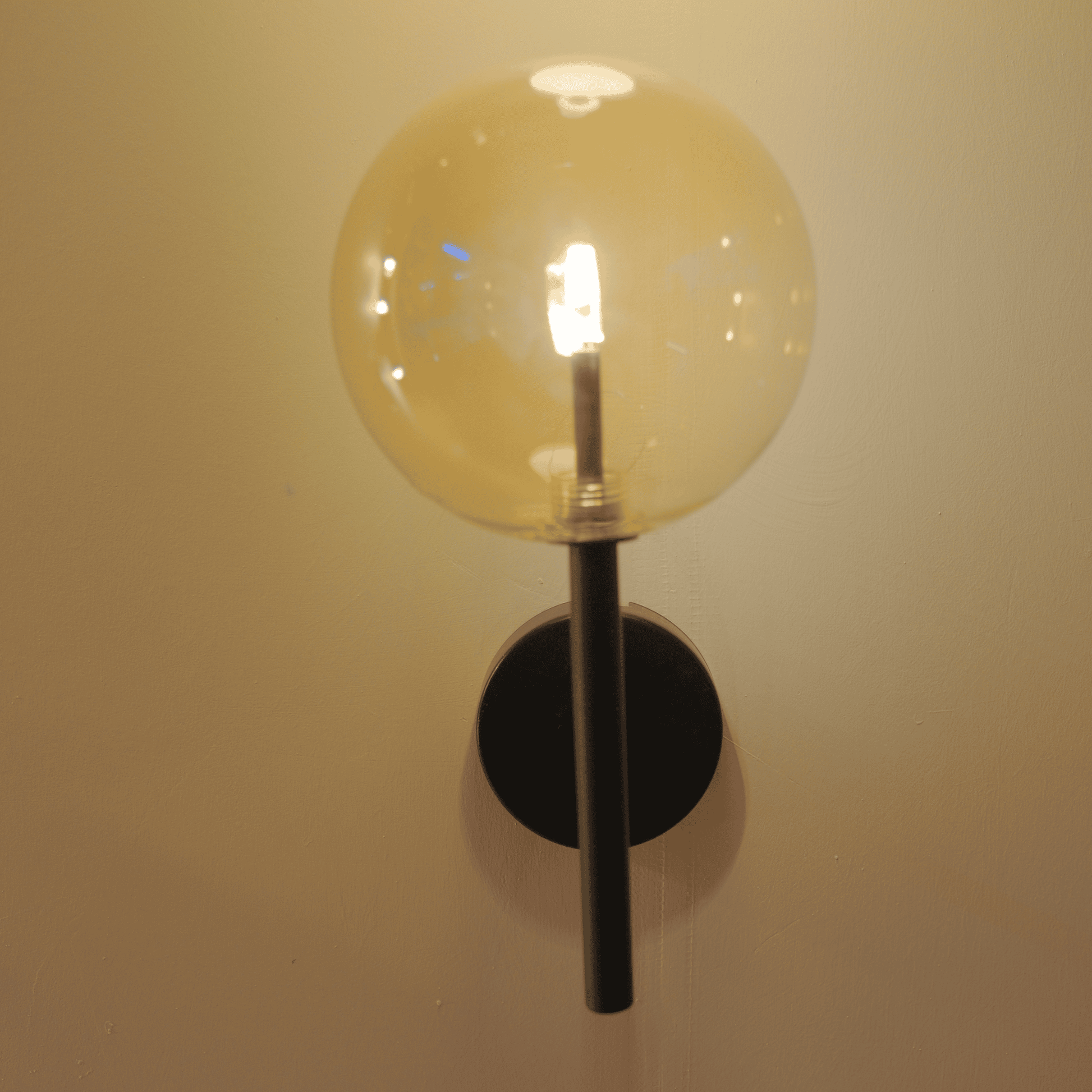 Modern black wall sconce with a clear glass globe shade emitting warm LED light.