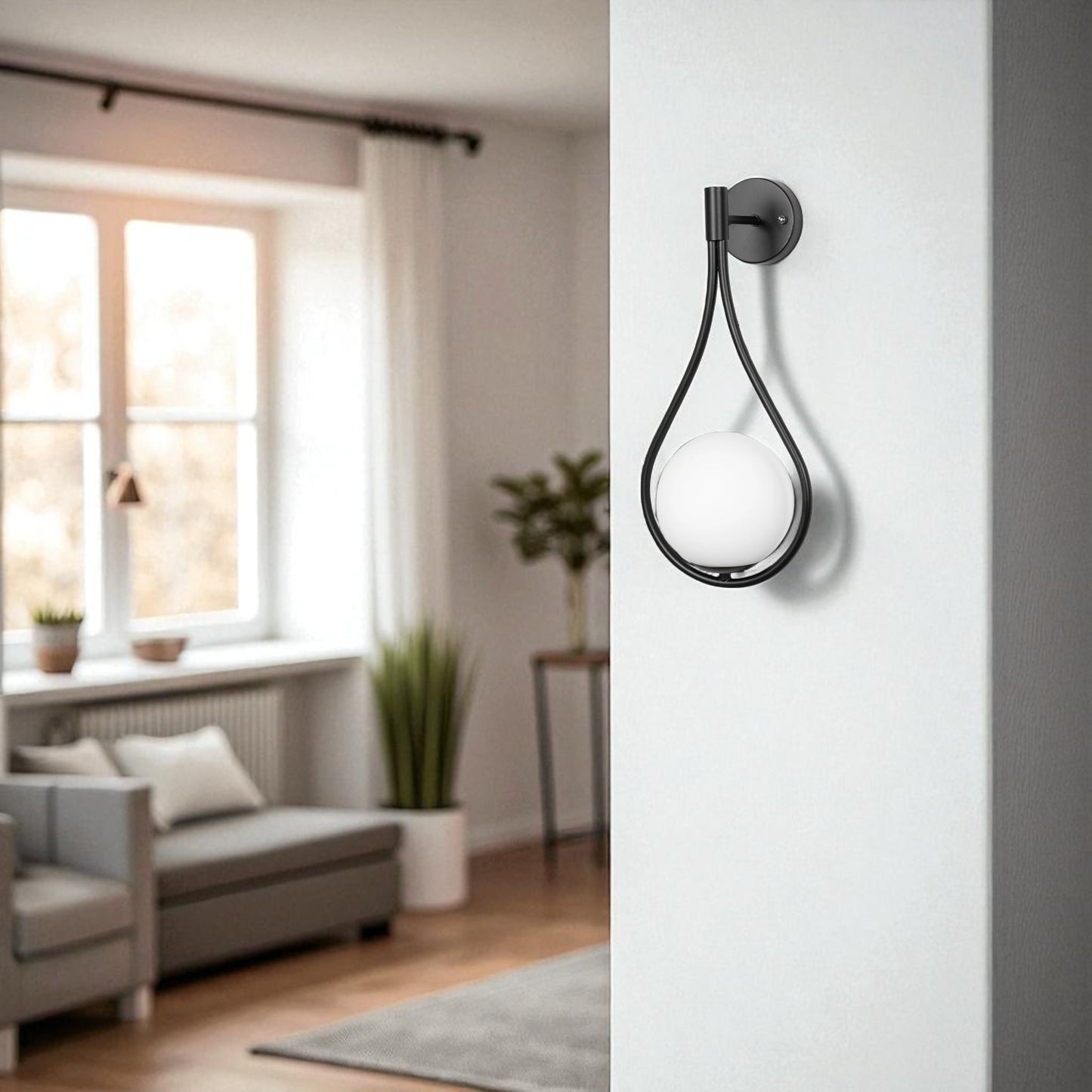 Modern matte black teardrop wall sconce with white globe light in a bright, minimalist living room.