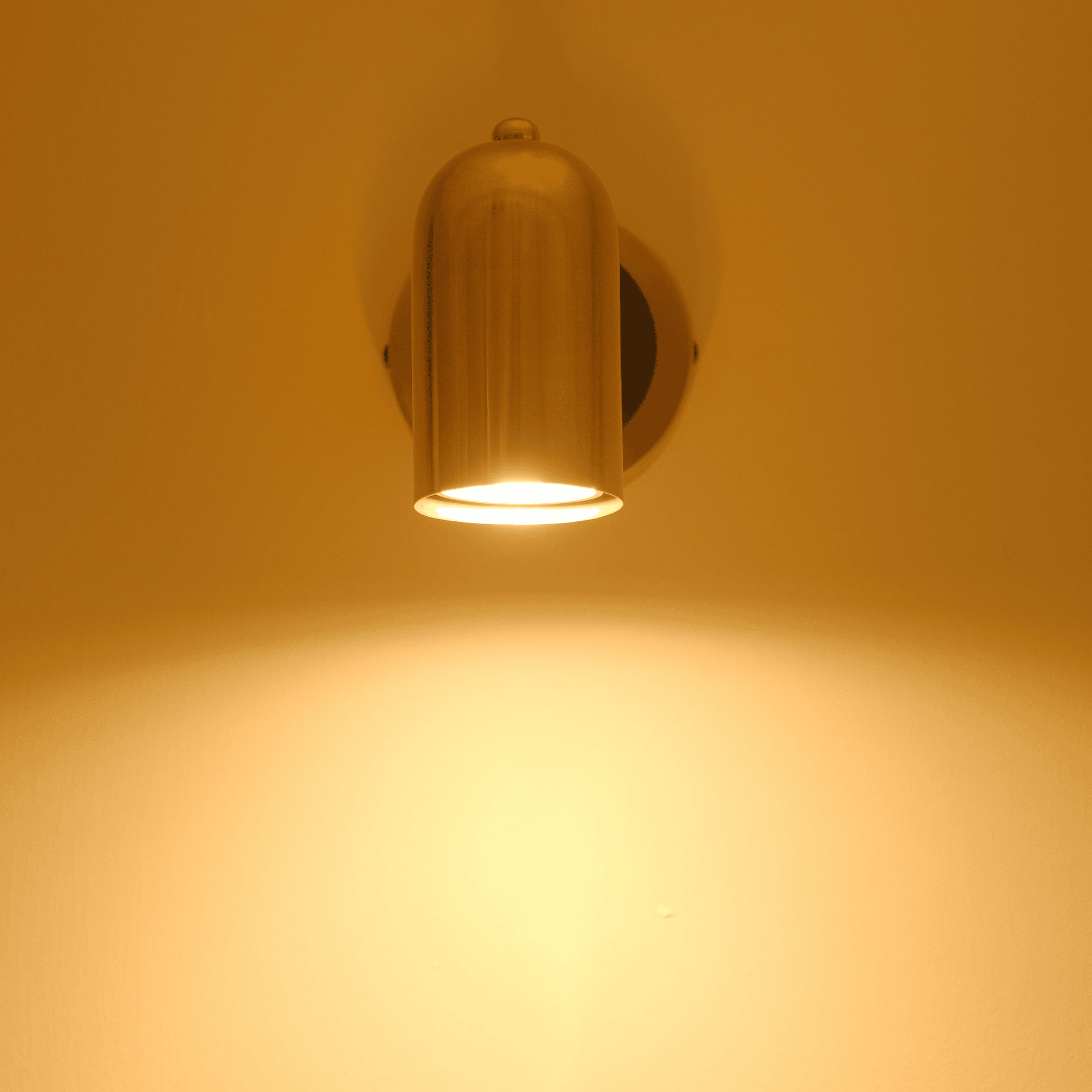 Brass cylinder wall sconce with warm downward light on an interior wall.