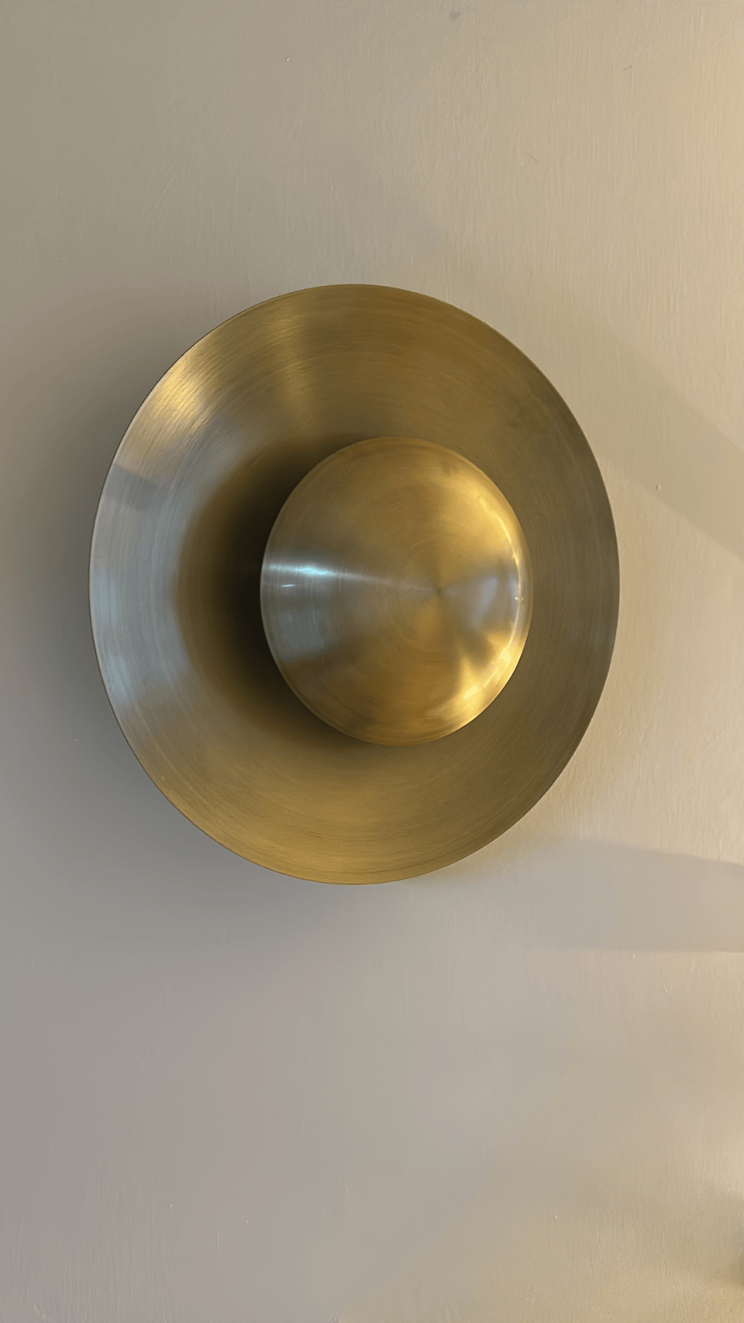 Modern brass disc wall sconce with a sculptural concentric design that enhances ambient interior lighting.