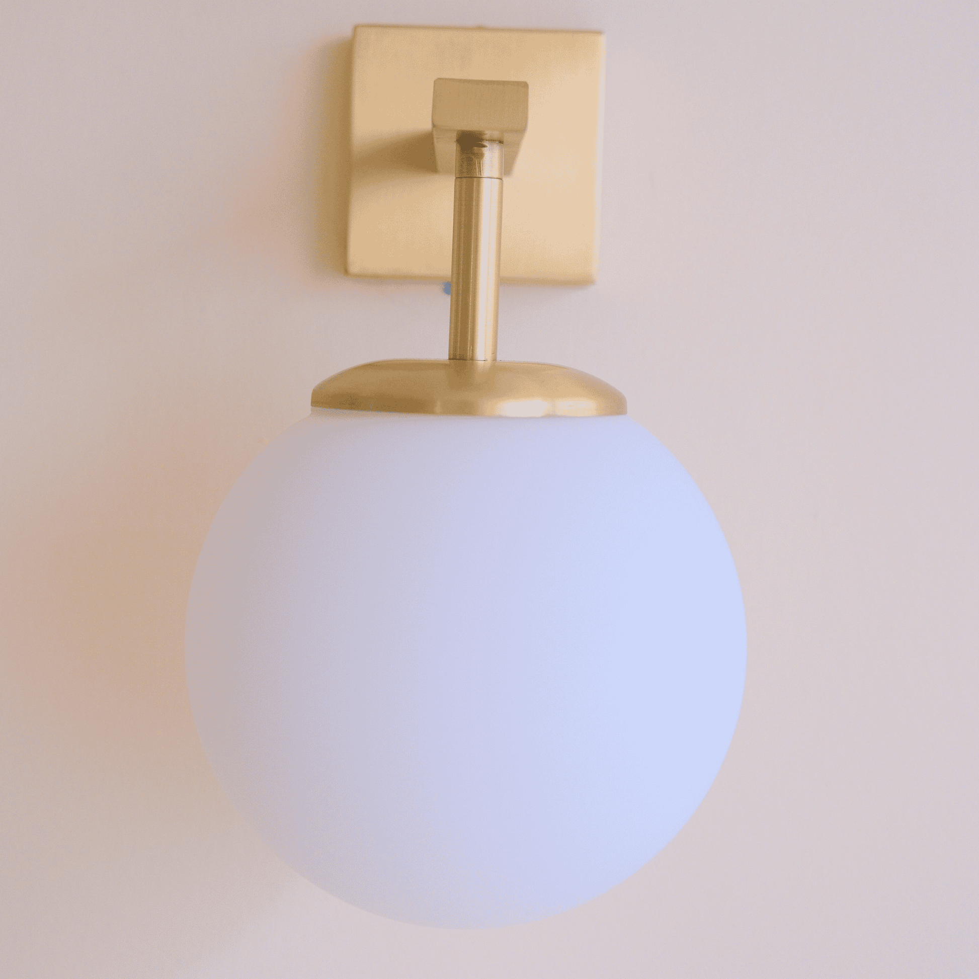 Modern brass wall sconce with a frosted globe shade mounted on a neutral wall, designed for soft and stylish interior lighting.