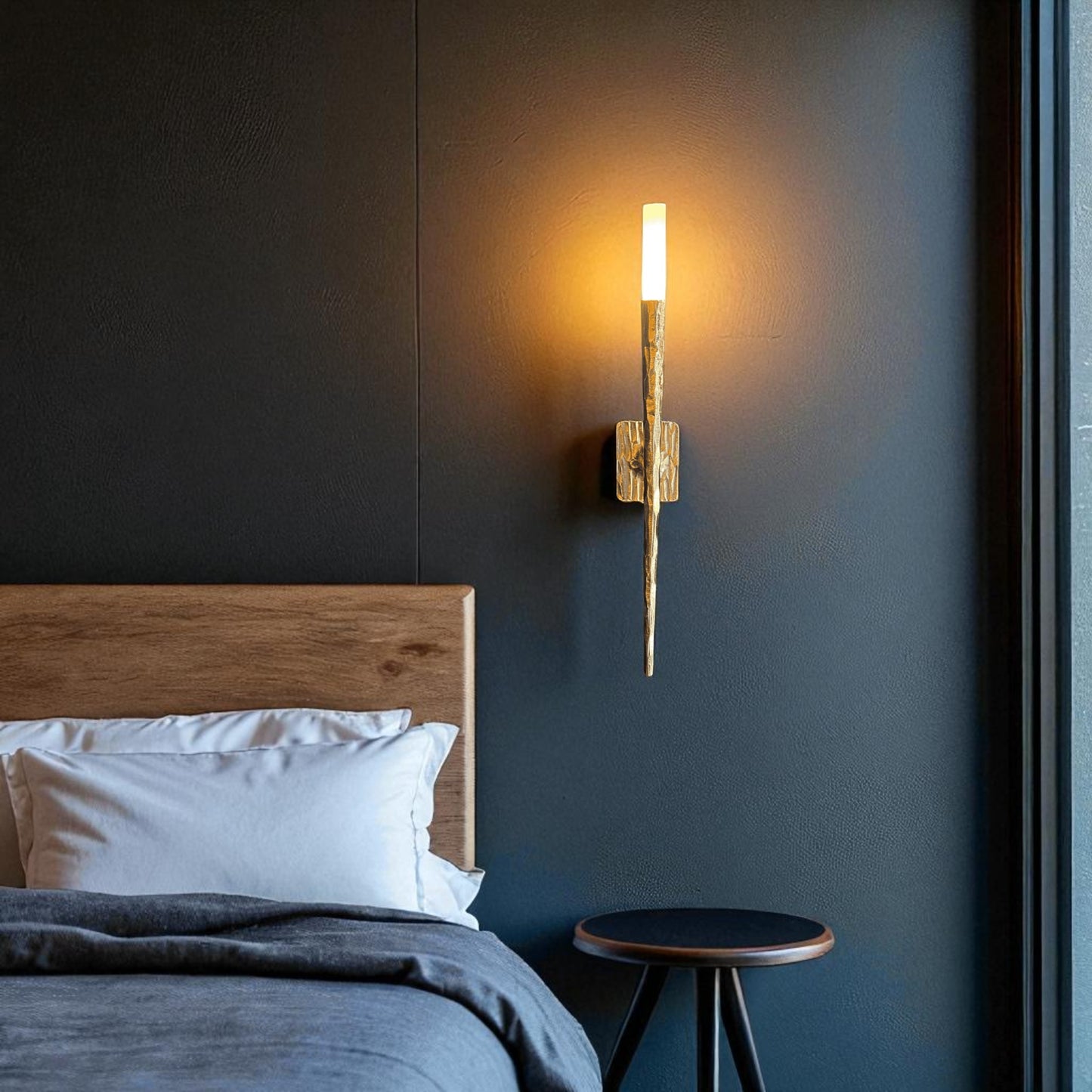 Modern brass wall sconce mounted beside a wooden bed, casting warm ambient light in a stylish bedroom setting.