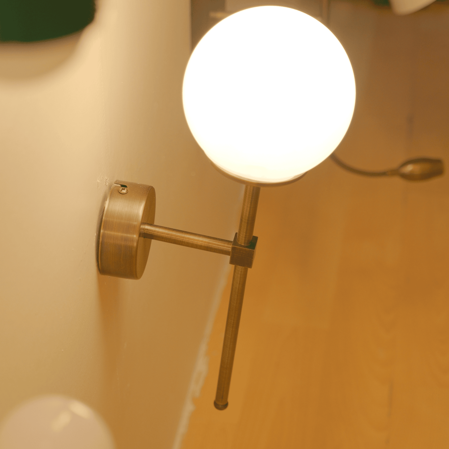Perspective view of modern brass wall sconce with downward-facing frosted globe on light-colored wall.