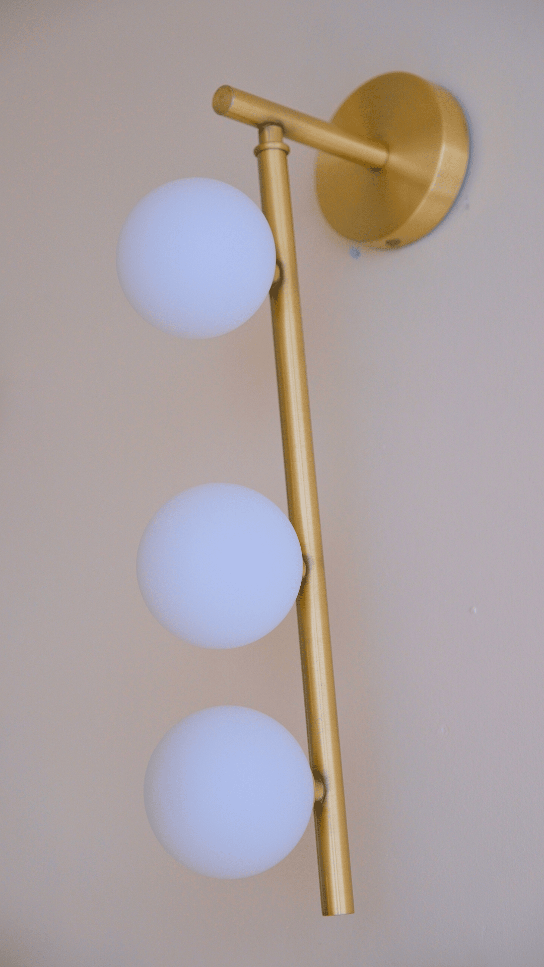 Modern brass wall sconce with three opal glass globes arranged vertically for soft ambient lighting.