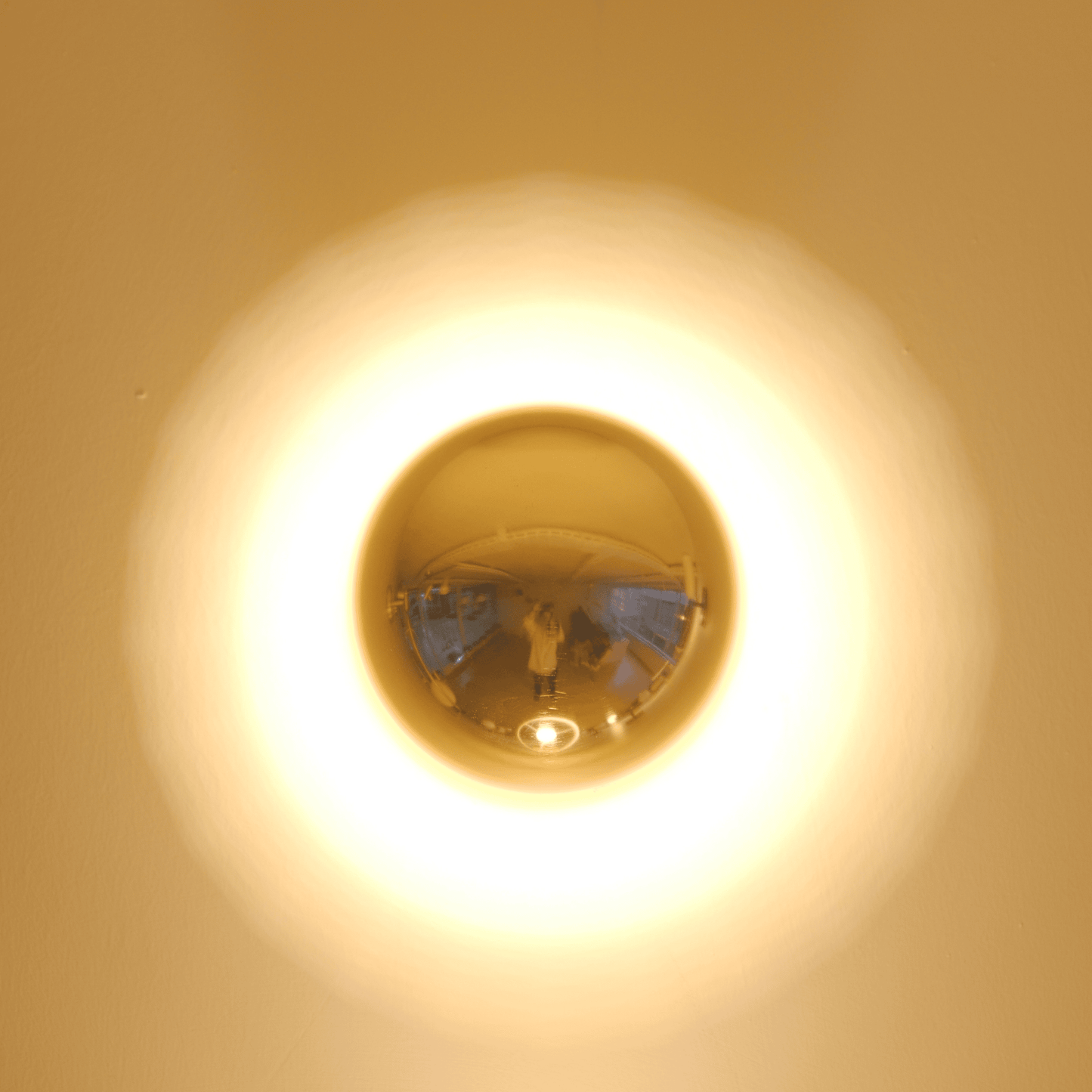 A brass wall sconce emits a circular ambient glow, ideal for modern interior lighting design.