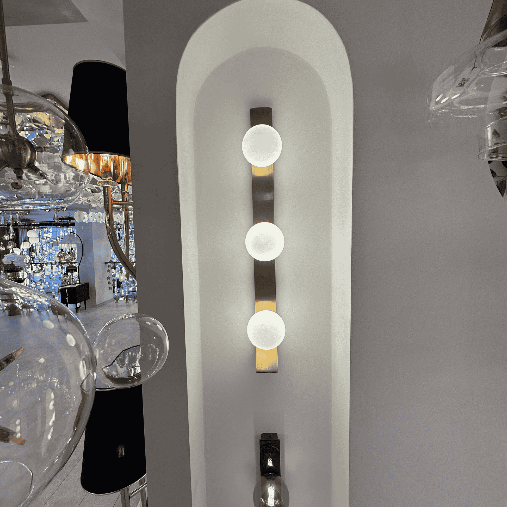 Modern brass wall sconce with three opal glass globes installed in a white arched wall niche.