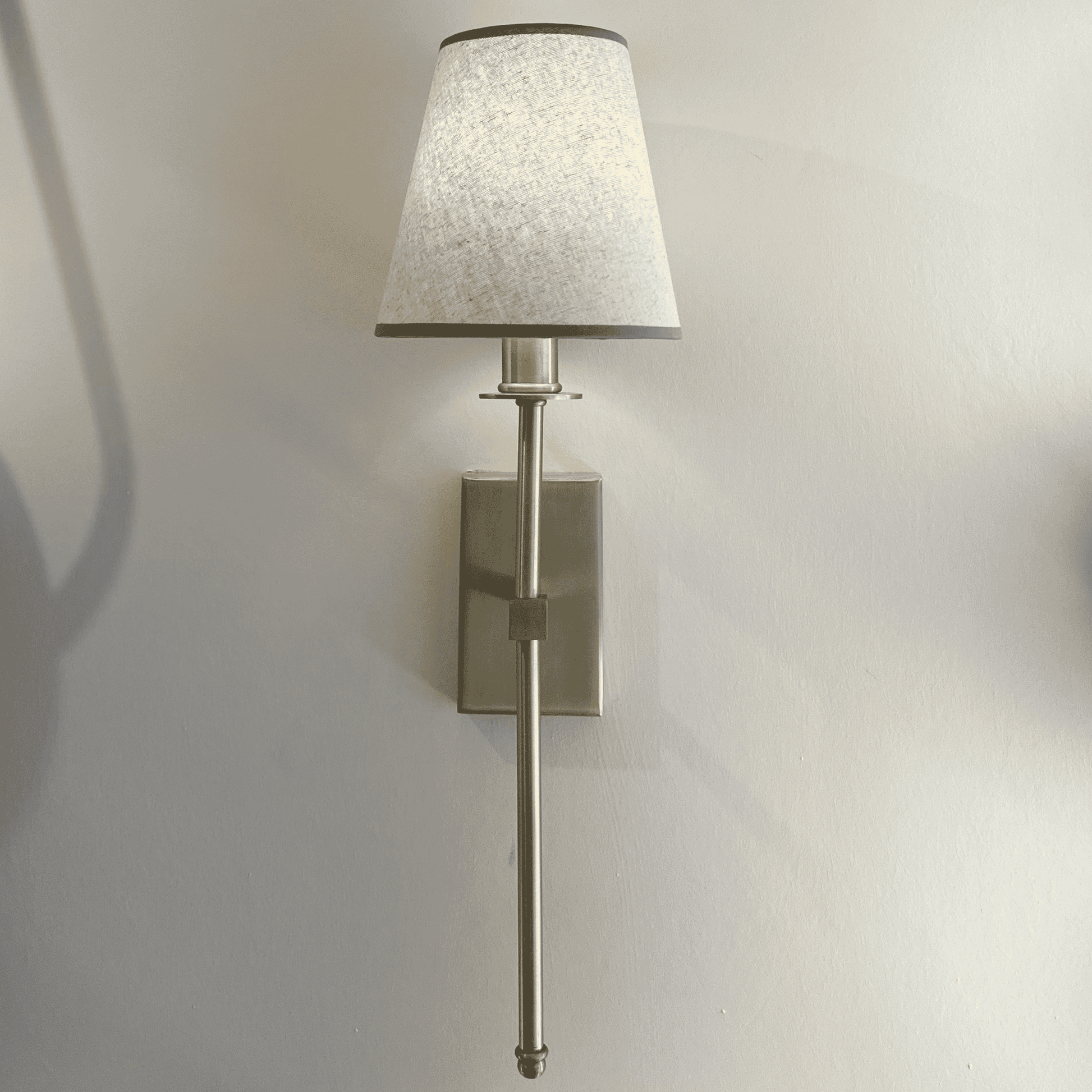 Brass wall sconce with fabric shade mounted among other fixtures in a contemporary lighting showroom display.