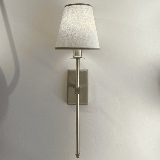 Brass wall sconce with fabric shade mounted among other fixtures in a contemporary lighting showroom display.