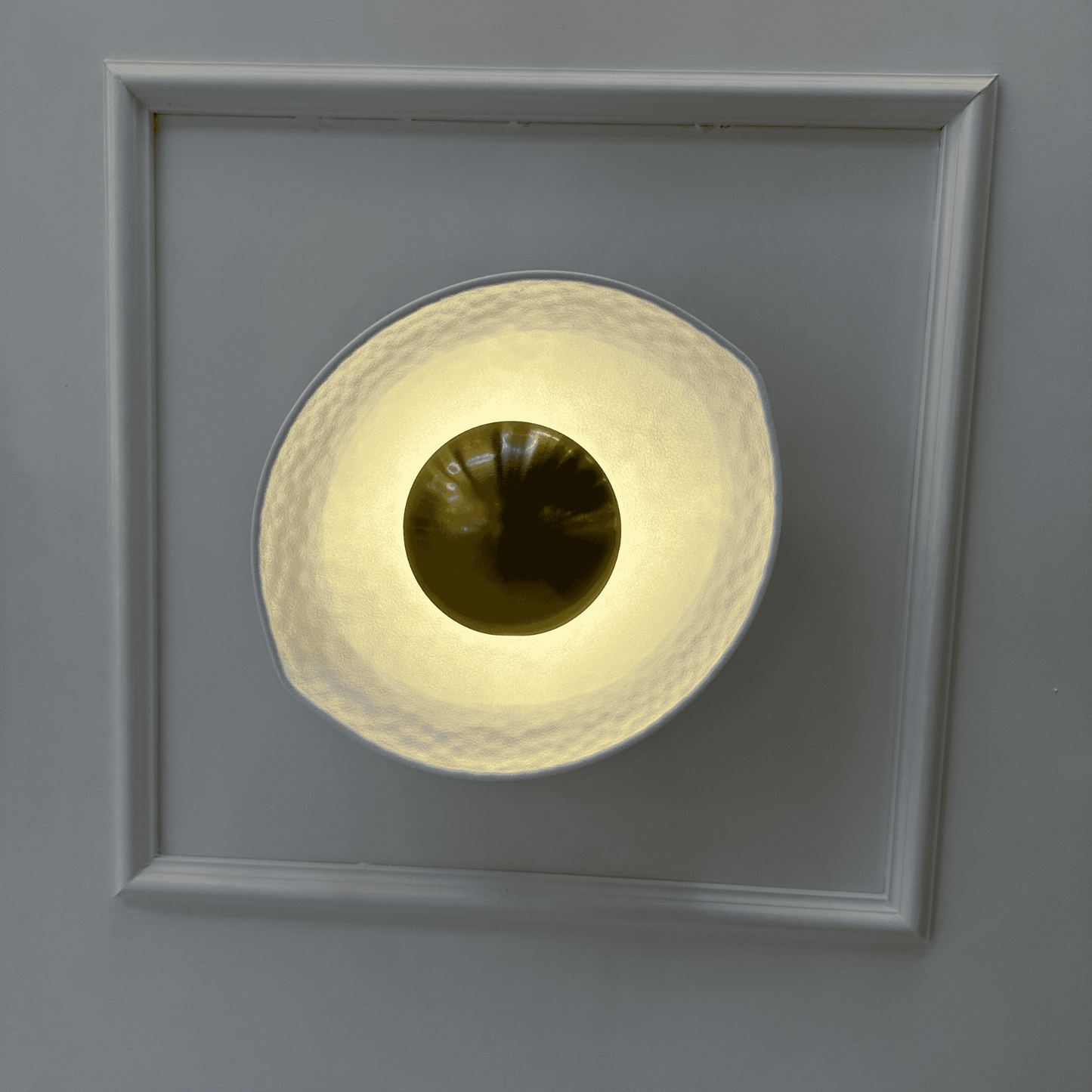 Front view of a white and gold deco wall sconce with a hammered finish and golden dome, emitting soft ambient light.