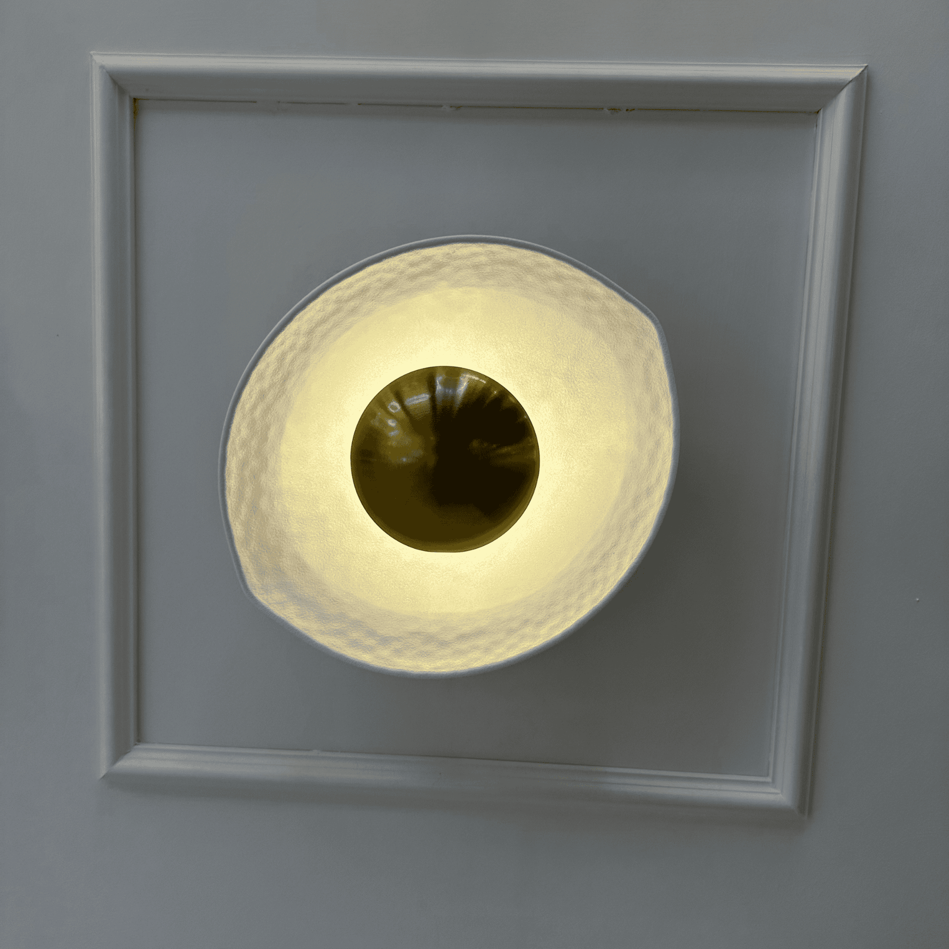 Front view of a white and gold deco wall sconce with a hammered finish and golden dome, emitting soft ambient light.