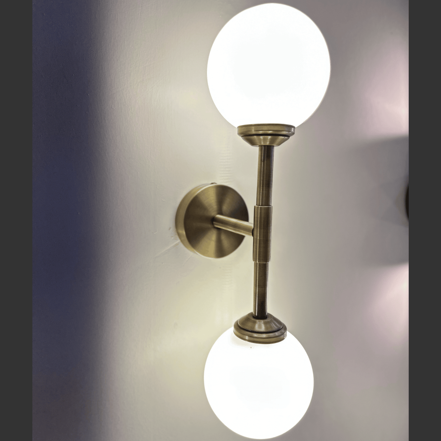 Wall-mounted light fixture with two round glass shades on a neutral background