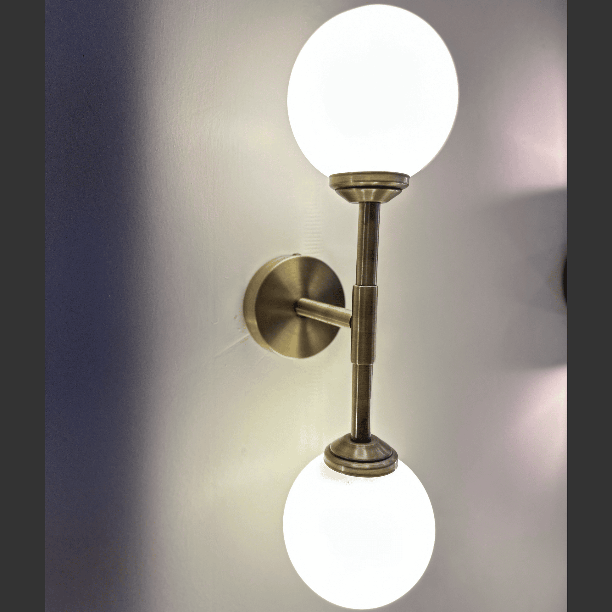 Wall-mounted light fixture with two round glass shades on a neutral background