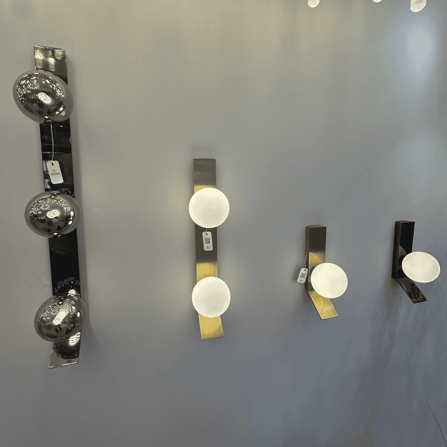 Wall display of brass and black sconces with frosted and smoked globe shades in a lighting showroom.