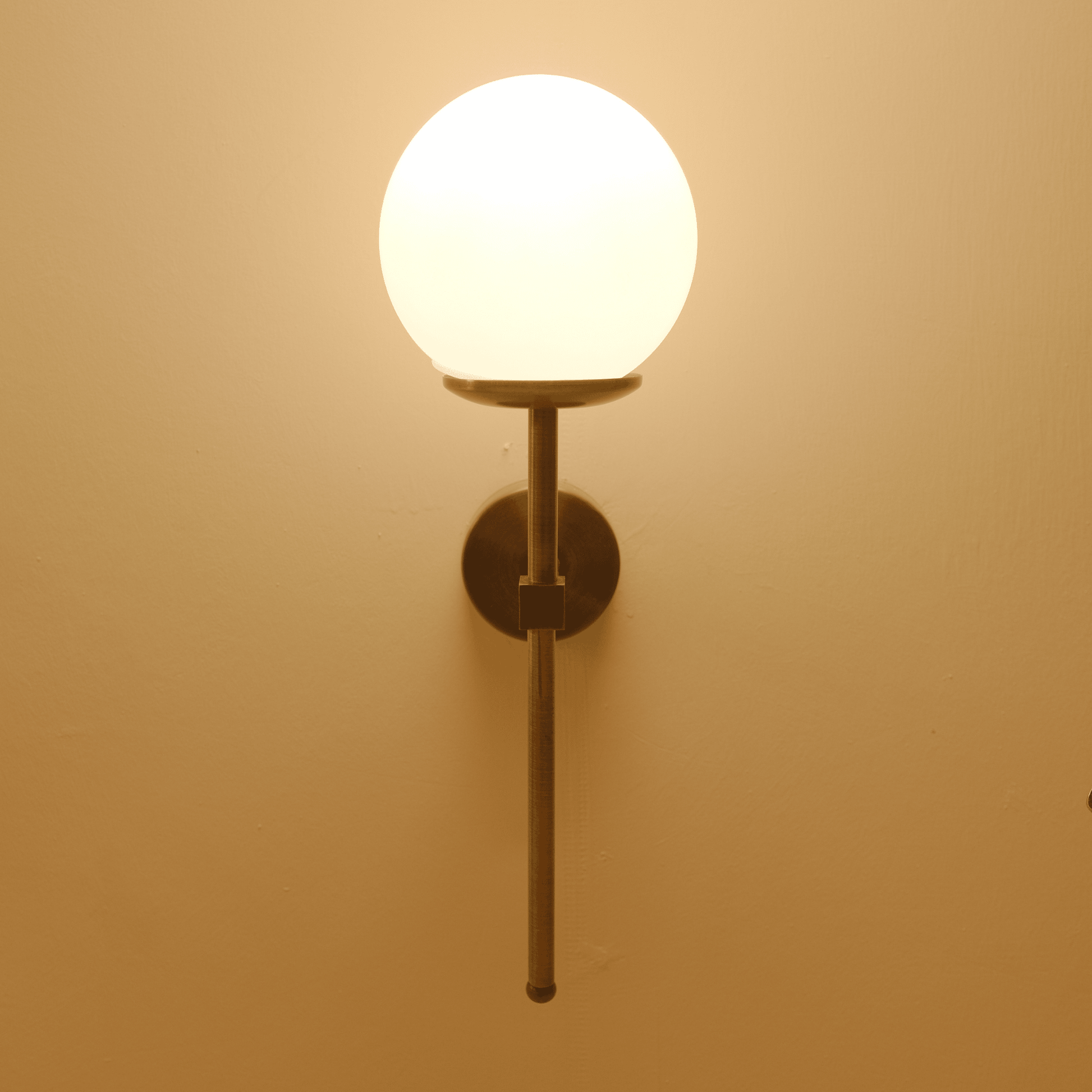 Front-facing image of a modern brass wall sconce with a frosted globe shade emitting soft ambient light.