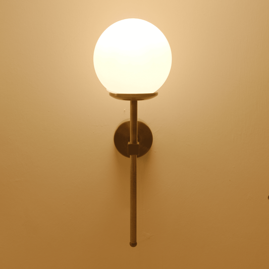 Front-facing image of a modern brass wall sconce with a frosted globe shade emitting soft ambient light.