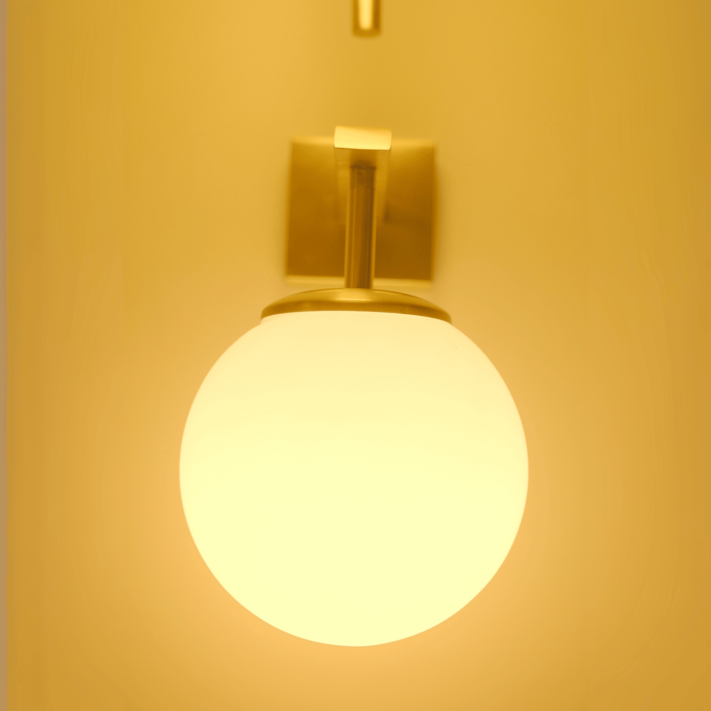Brass wall sconce with an upward opal globe shade emitting warm ambient light.