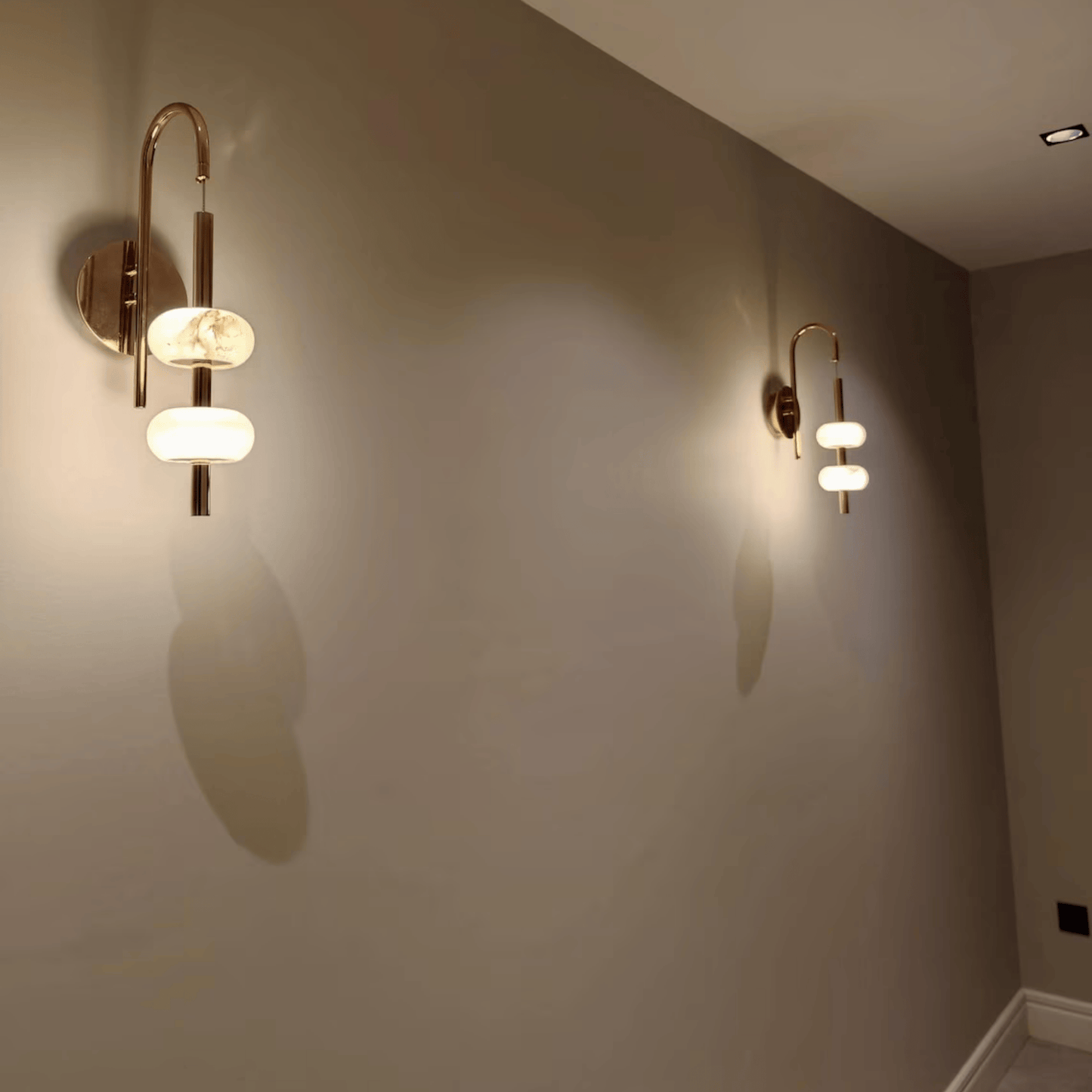 Two alabaster wall sconces with brass arms illuminating a modern hallway.