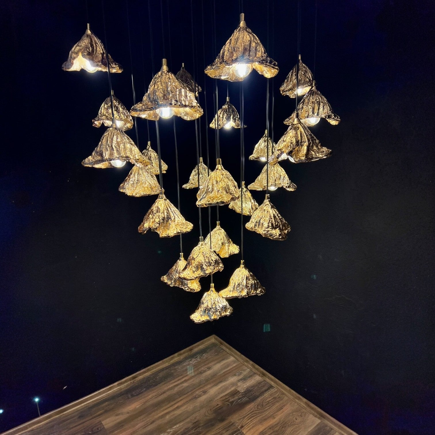 A cluster of sculptural leaf pendant lights with gold textured shades, suspended against a dark background to emphasize modern interior lighting design.