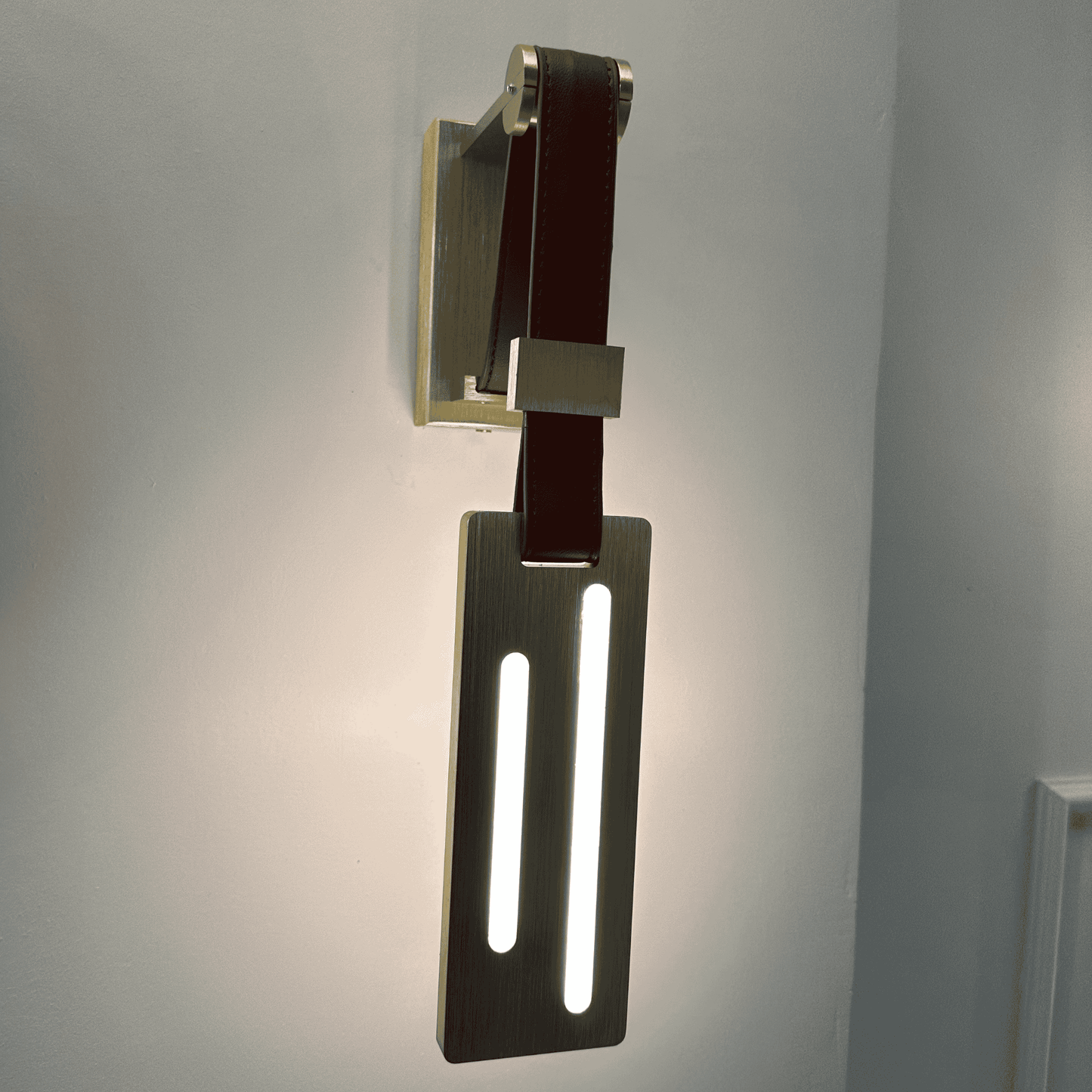 Modern leather wall sconce with vertical LED strip lights mounted on a brushed brass plate