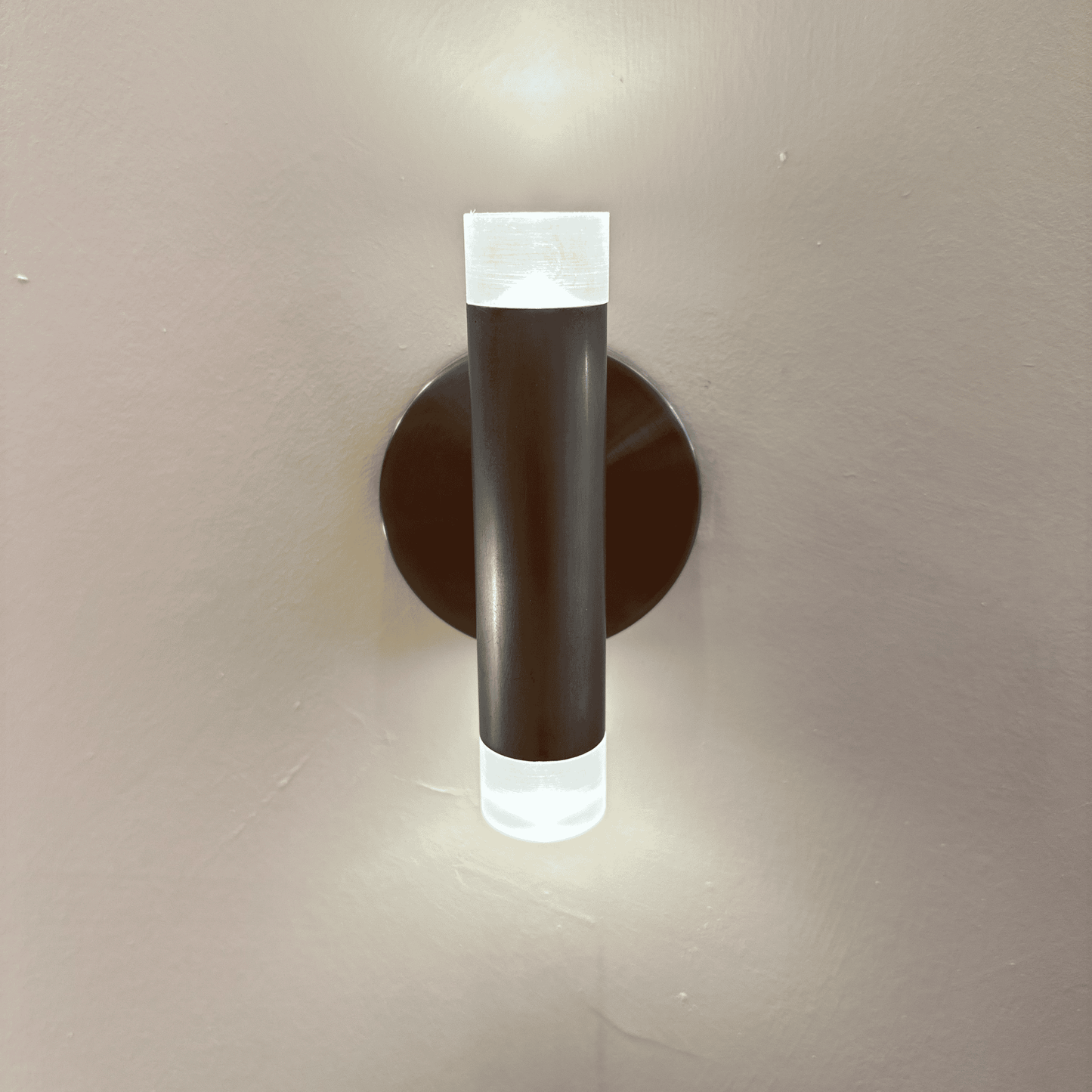 Modern LED wall sconce with brushed nickel finish and frosted acrylic ends, mounted on a neutral wall for soft ambient lighting.