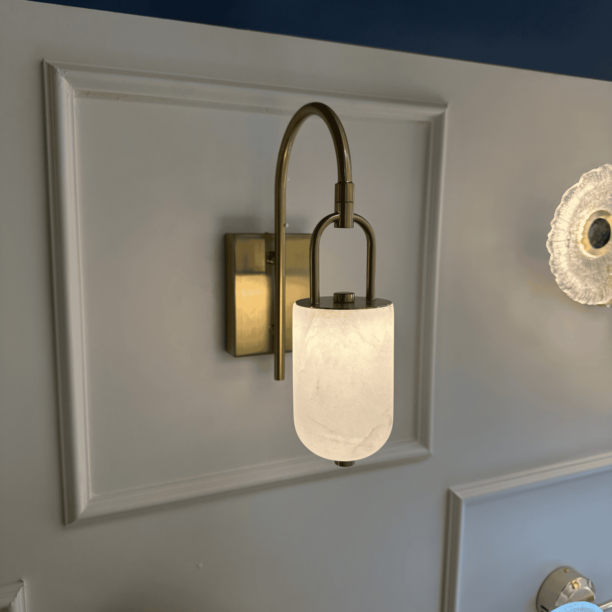 Side profile of modern marble wall sconce with curved brass arm and glowing alabaster shade.