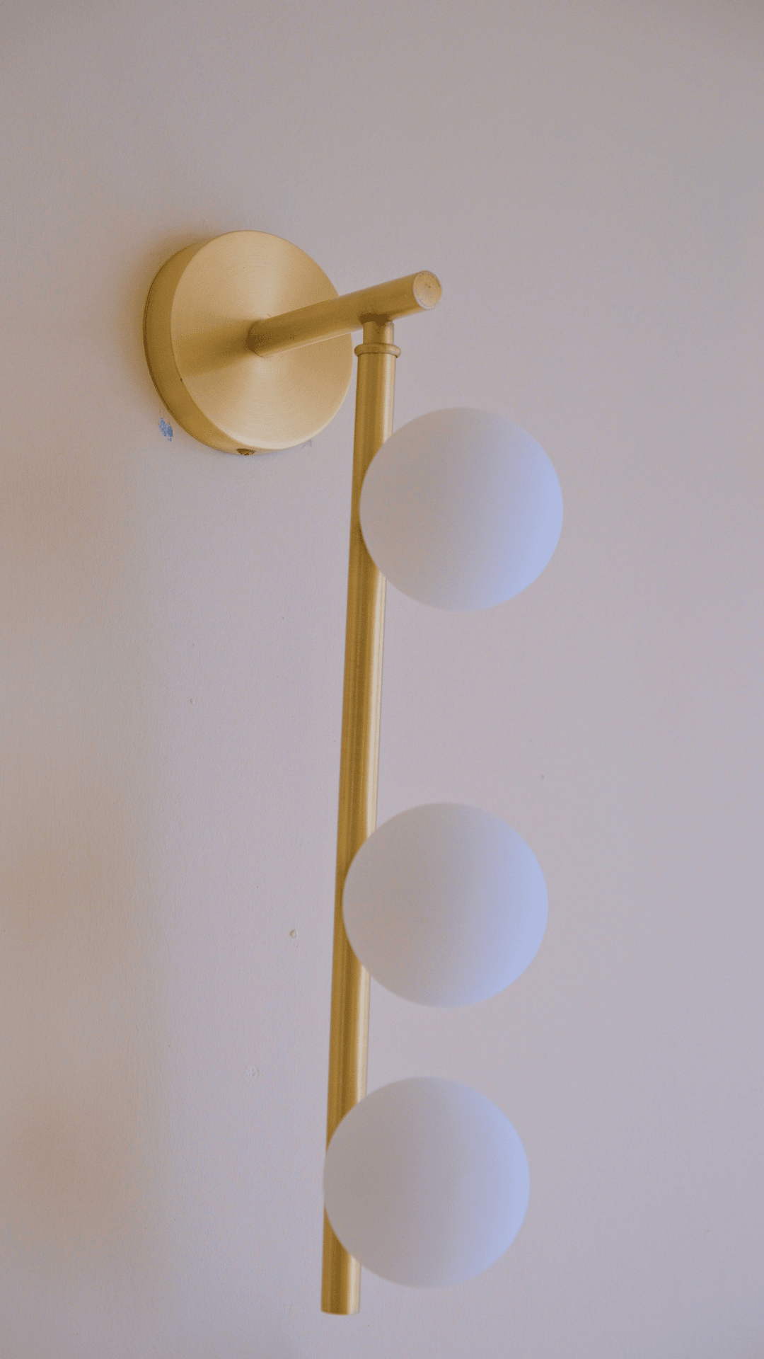 Contemporary brass wall light with three round opal globes providing soft ambient illumination.