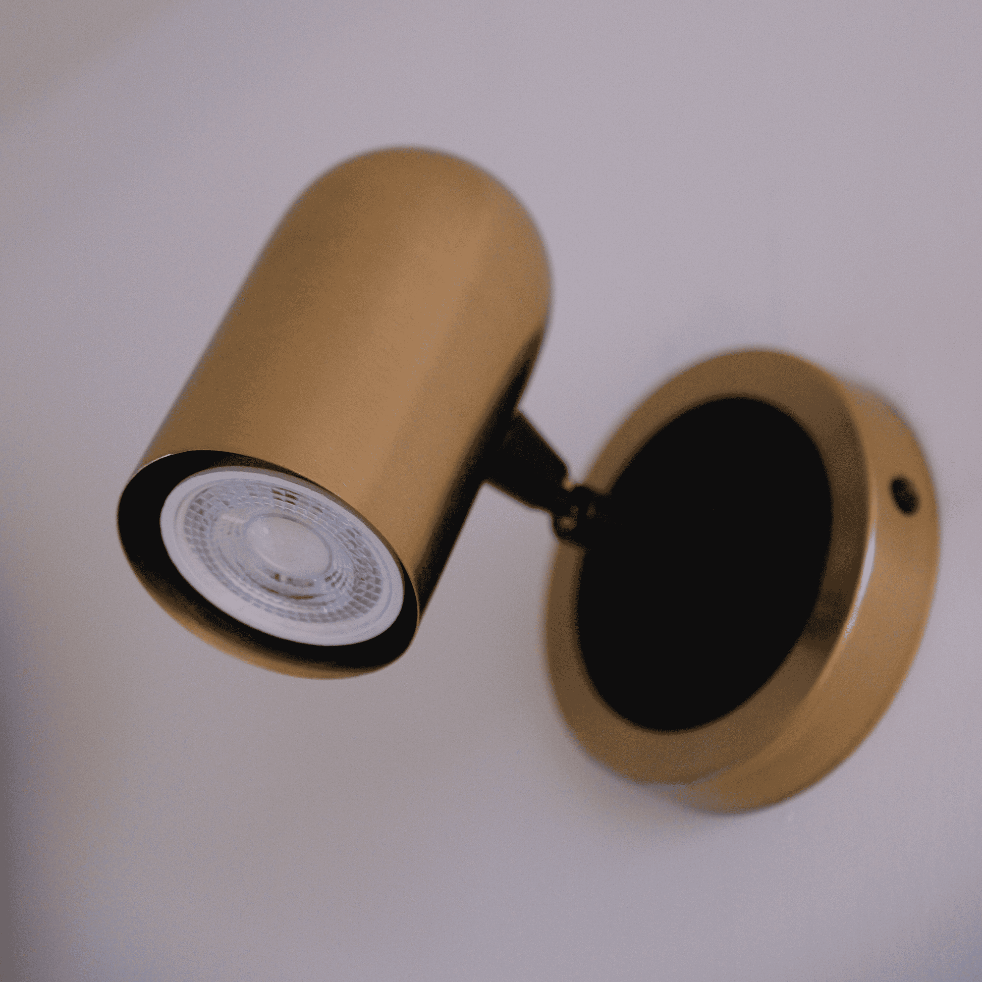 Wall-mounted brass cylinder sconce casting ambient light on a neutral wall.