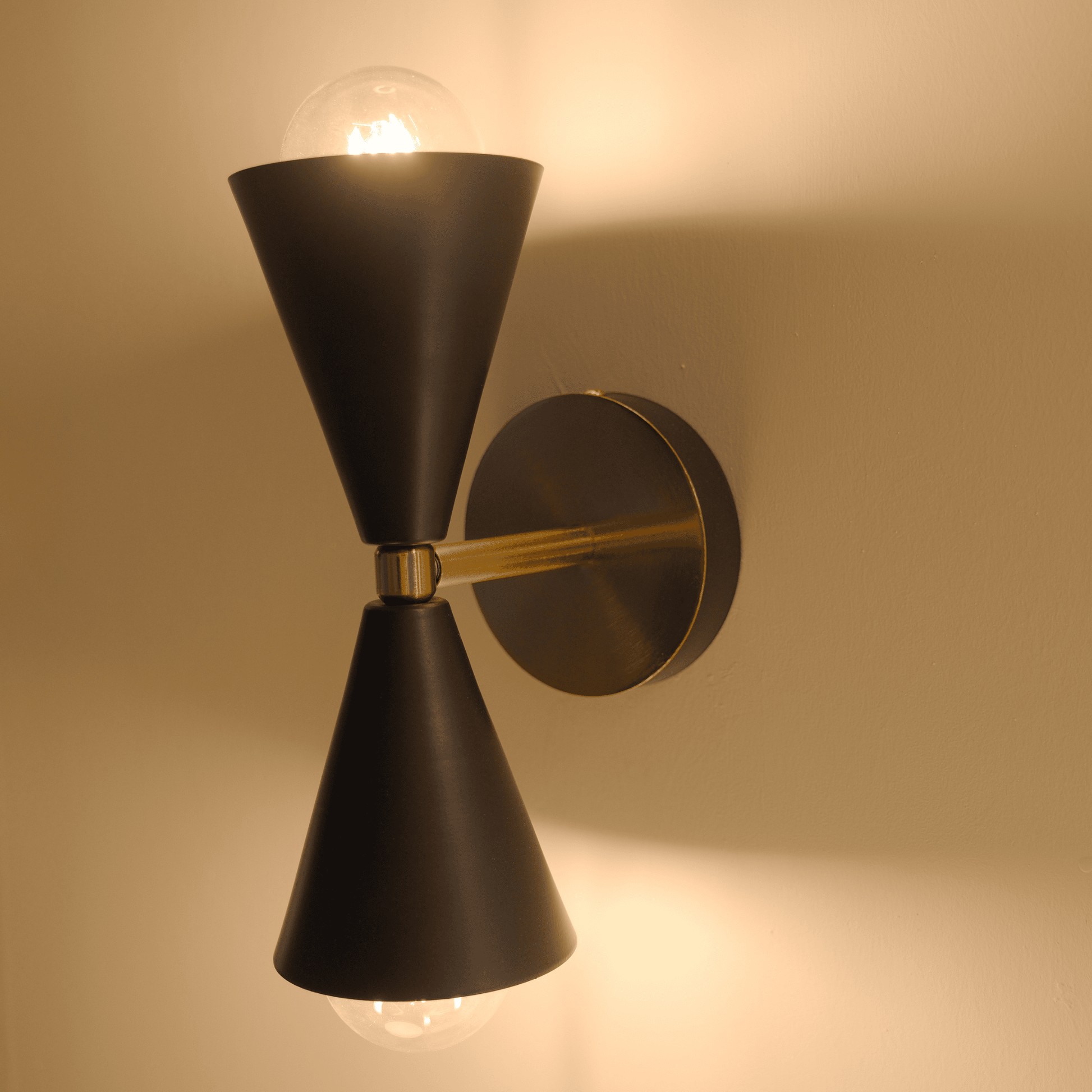 Black and brass cone wall sconce mounted on wall with light emitting both upward and downward.