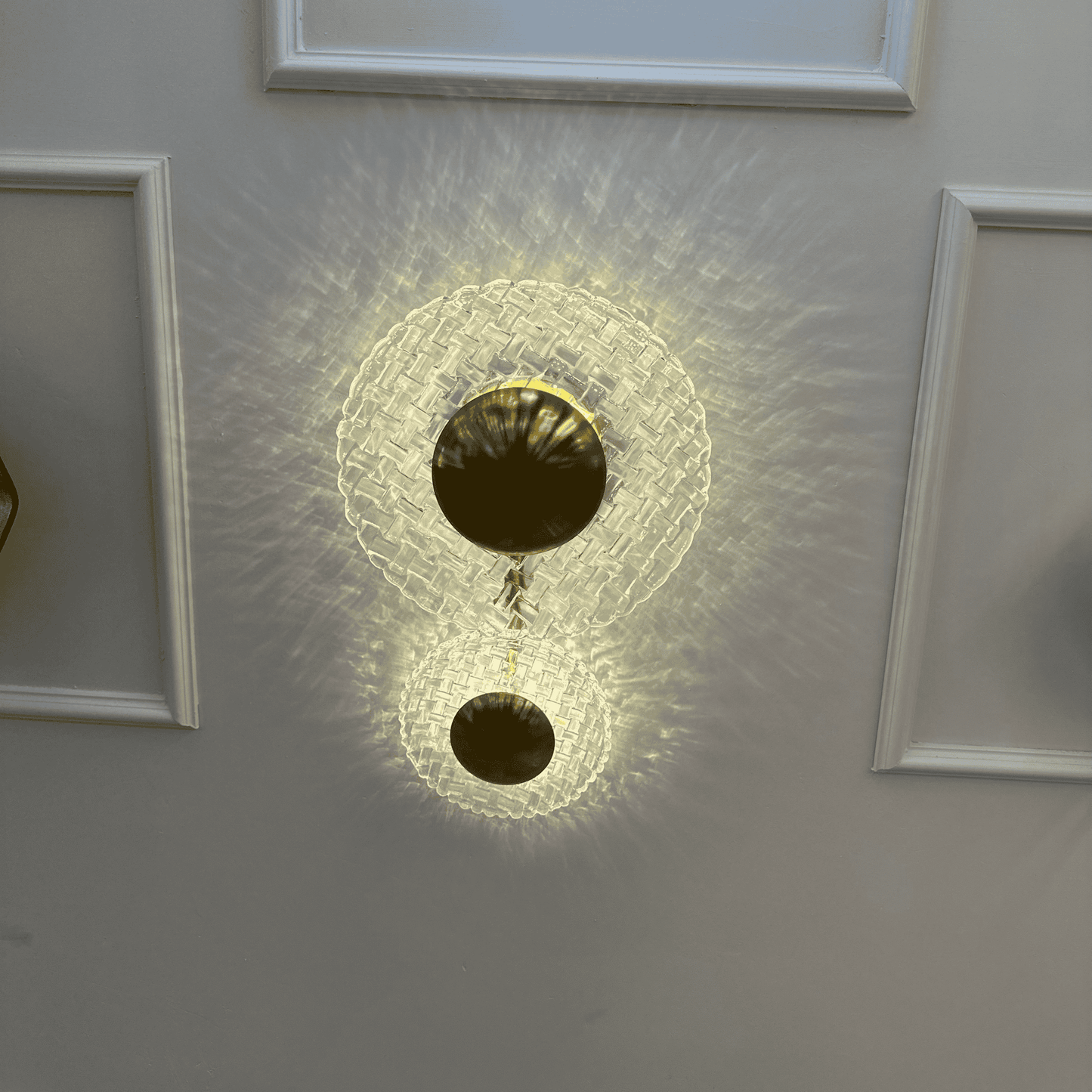 Modern brass and clear glass wall sconce casting patterned light on an entryway wall with classic molding.