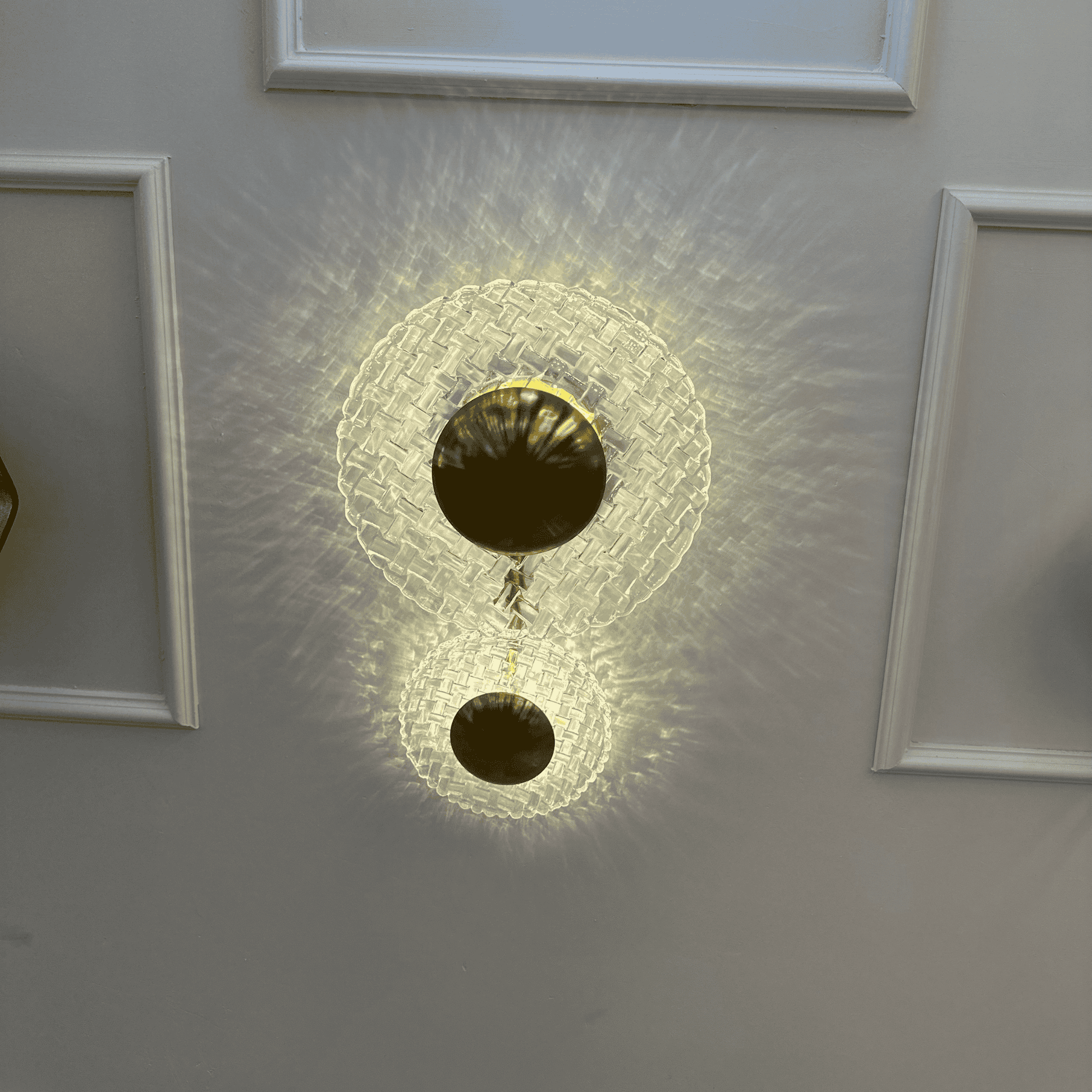 Modern brass and clear glass wall sconce casting patterned light on an entryway wall with classic molding.