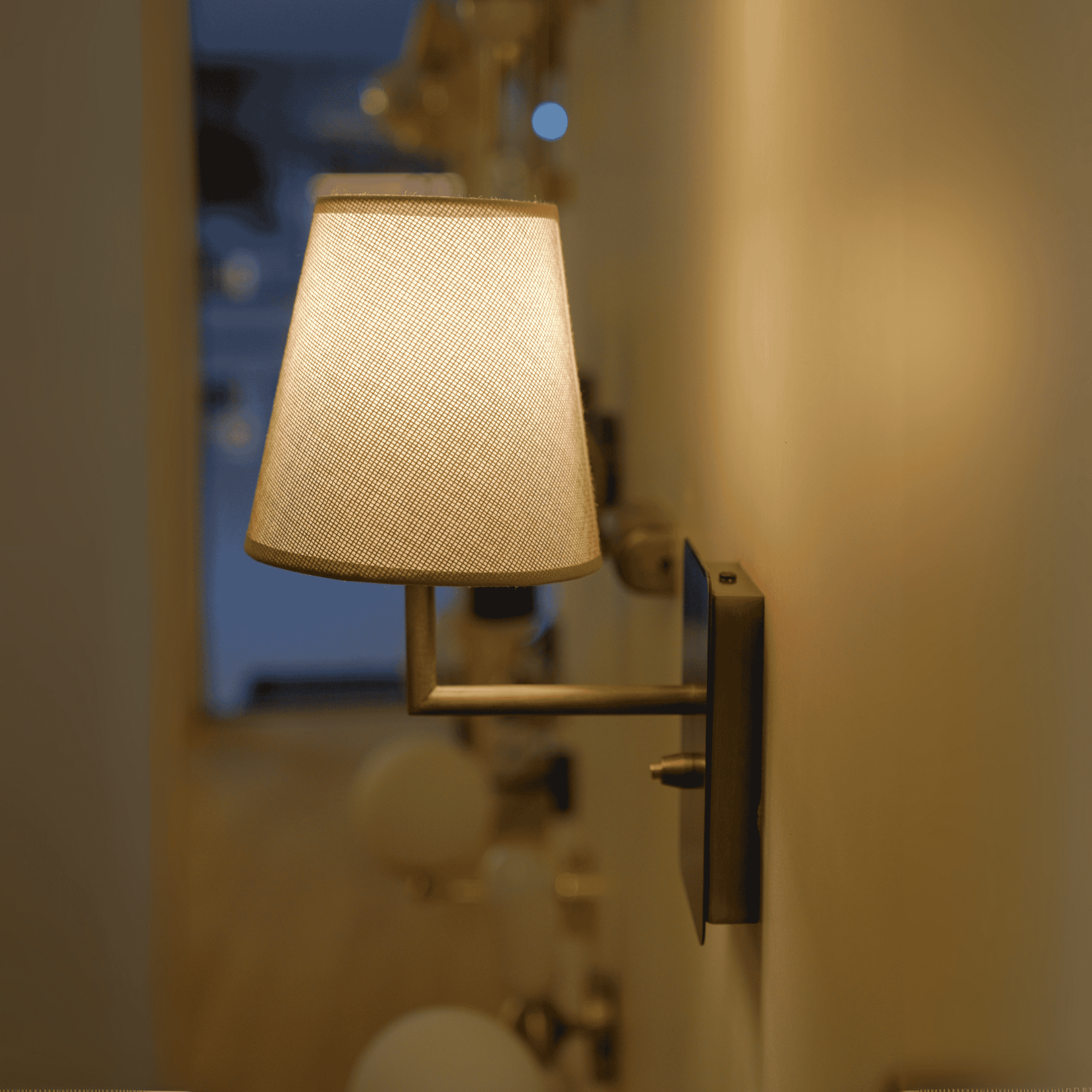 Modern brushed nickel wall sconce with a beige fabric shade, mounted in a softly lit hallway.