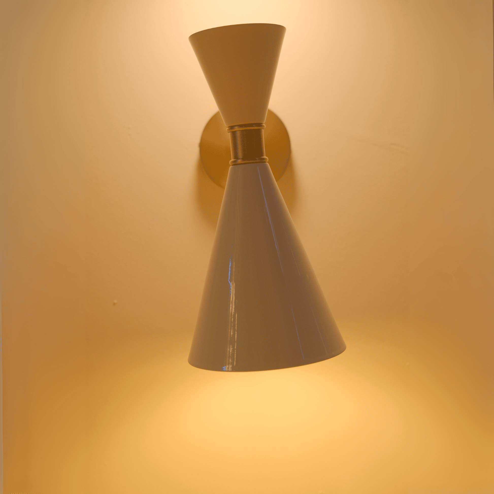 Modern white metal cone wall sconce emitting up and down light with warm ambient effect.