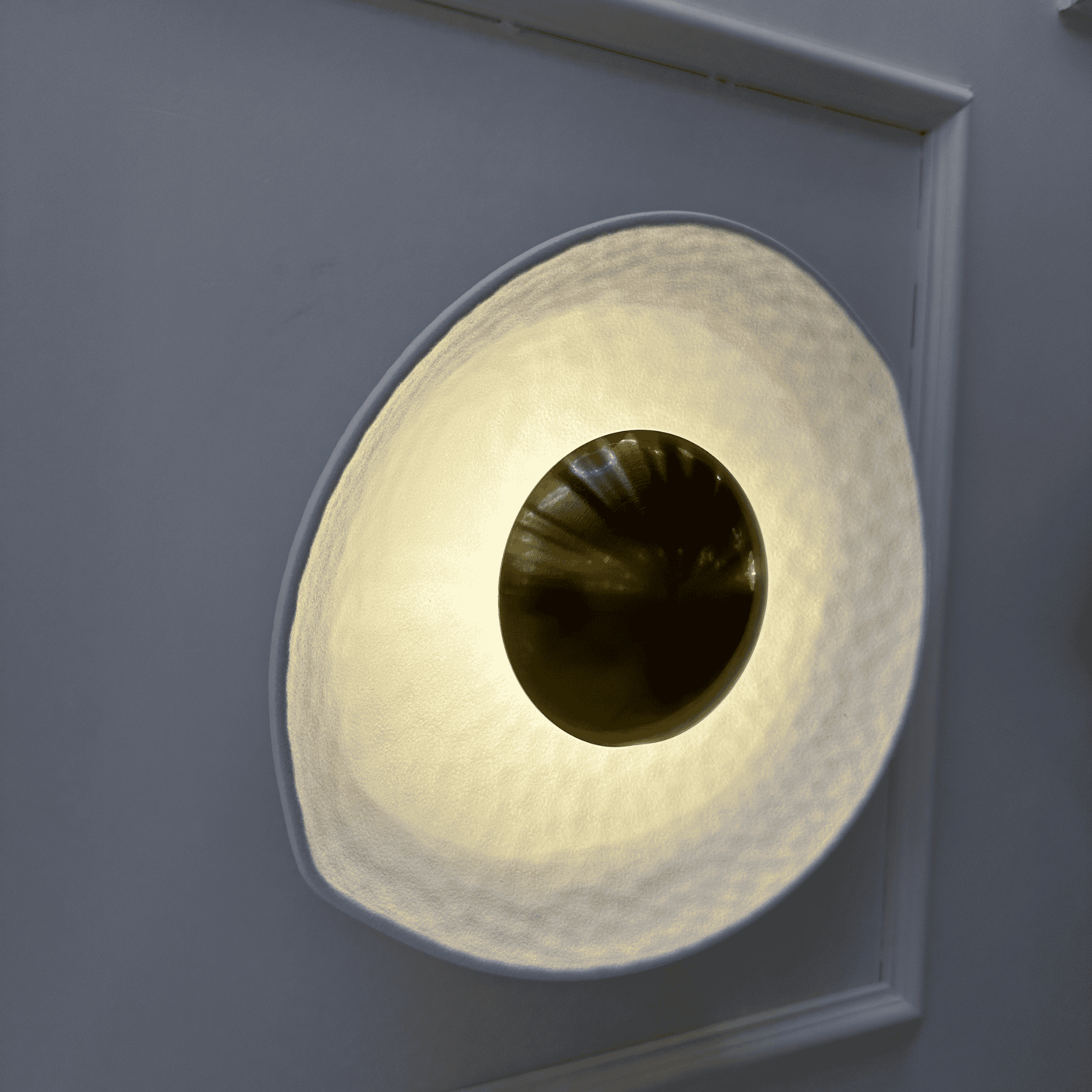 Oblique angle of a deco wall sconce with sculptural hammered white shade and central golden dome.