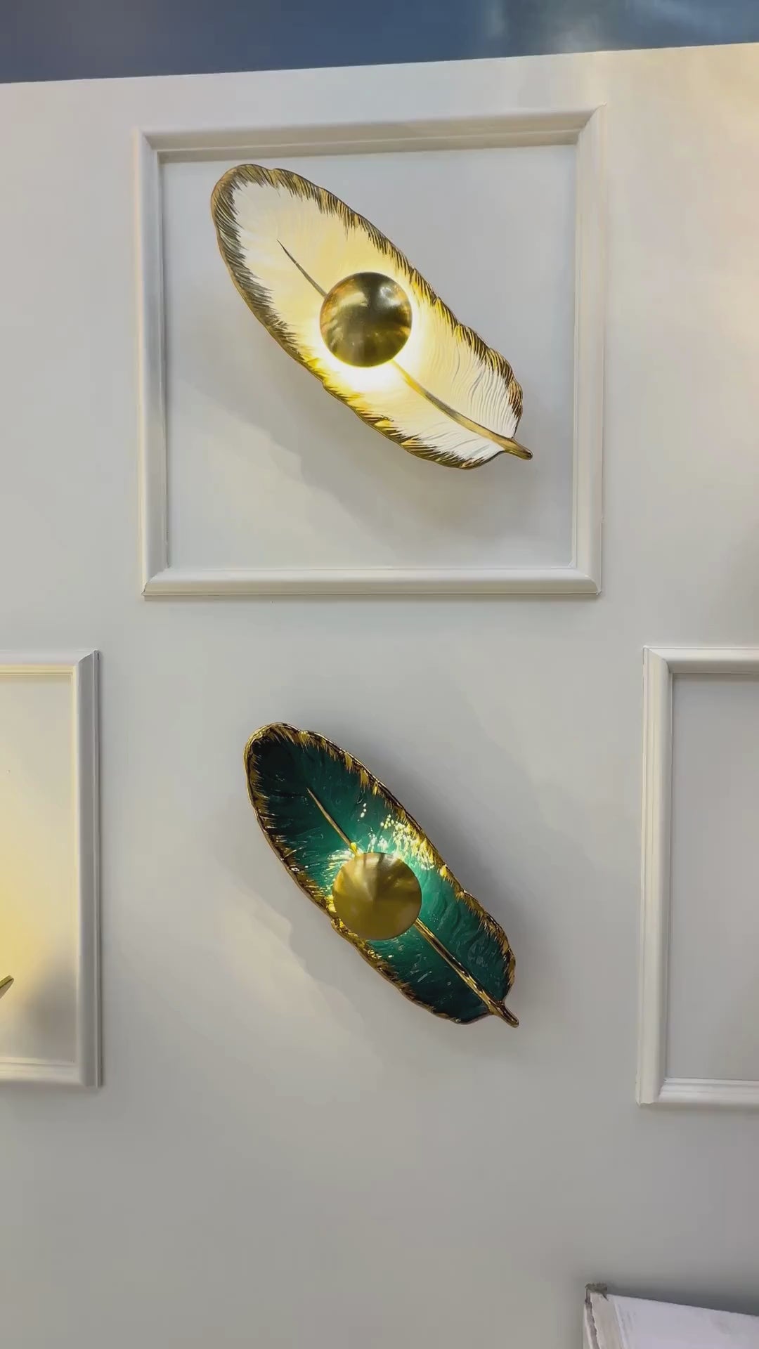 Horizontally placed feather wall light in emerald porcelain and brass finish with LED lighting, enhancing a contemporary interior wall.