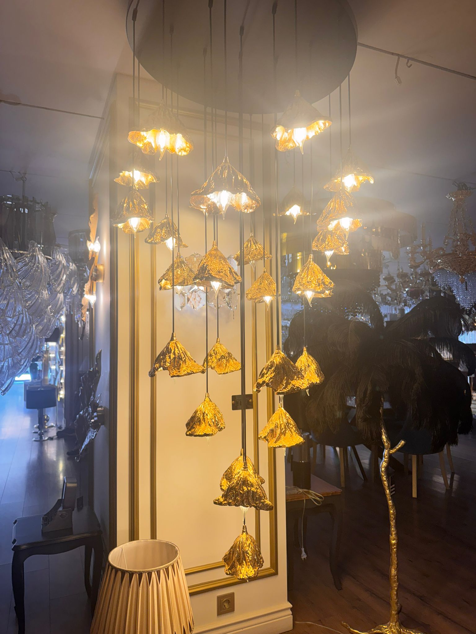 Bright pure brass leaf pendant lights forming a radiant chandelier in a luxury showroom.